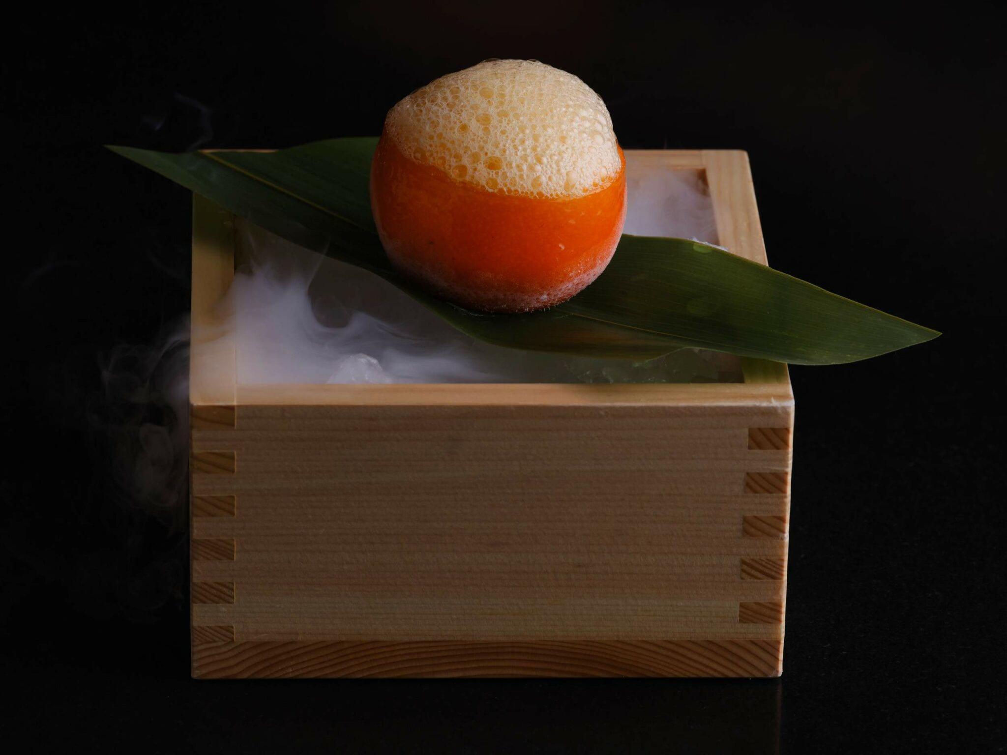 Contemporary plated dessert with apricot sphere, green leaf, and wooden base with dry ice