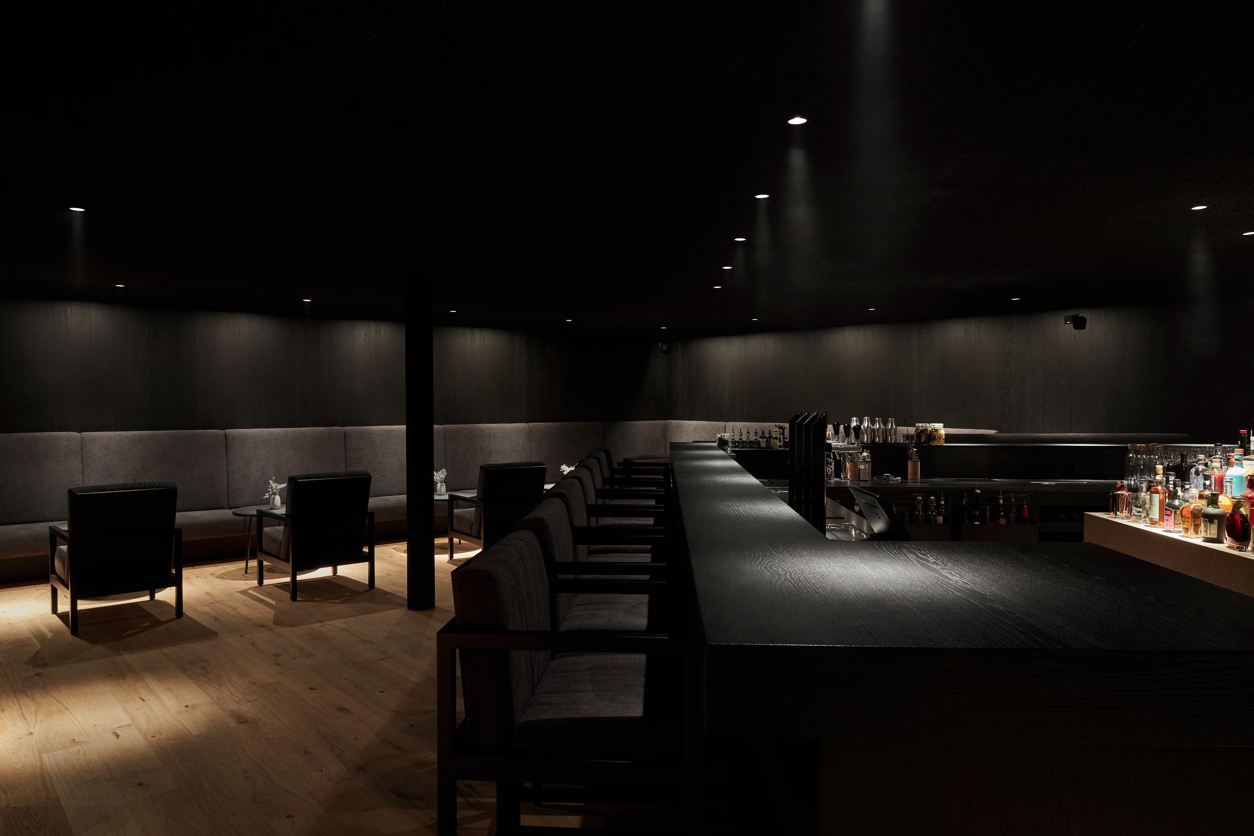 Forestis: a bar area in cool lighting with dark surfaces and backlighting, stone and modern architectural details