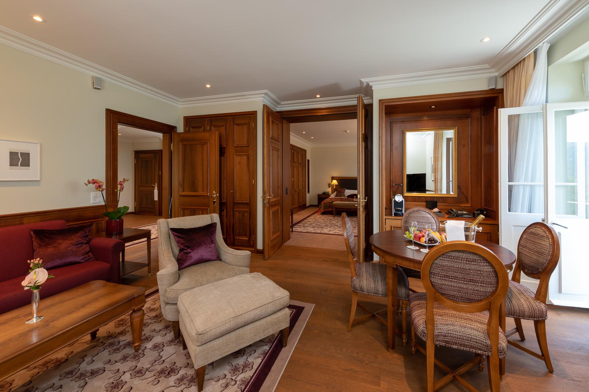 Suvretta House: a suite living area with wood parquet floors, sitting furniture, and multiple mountain-view windows