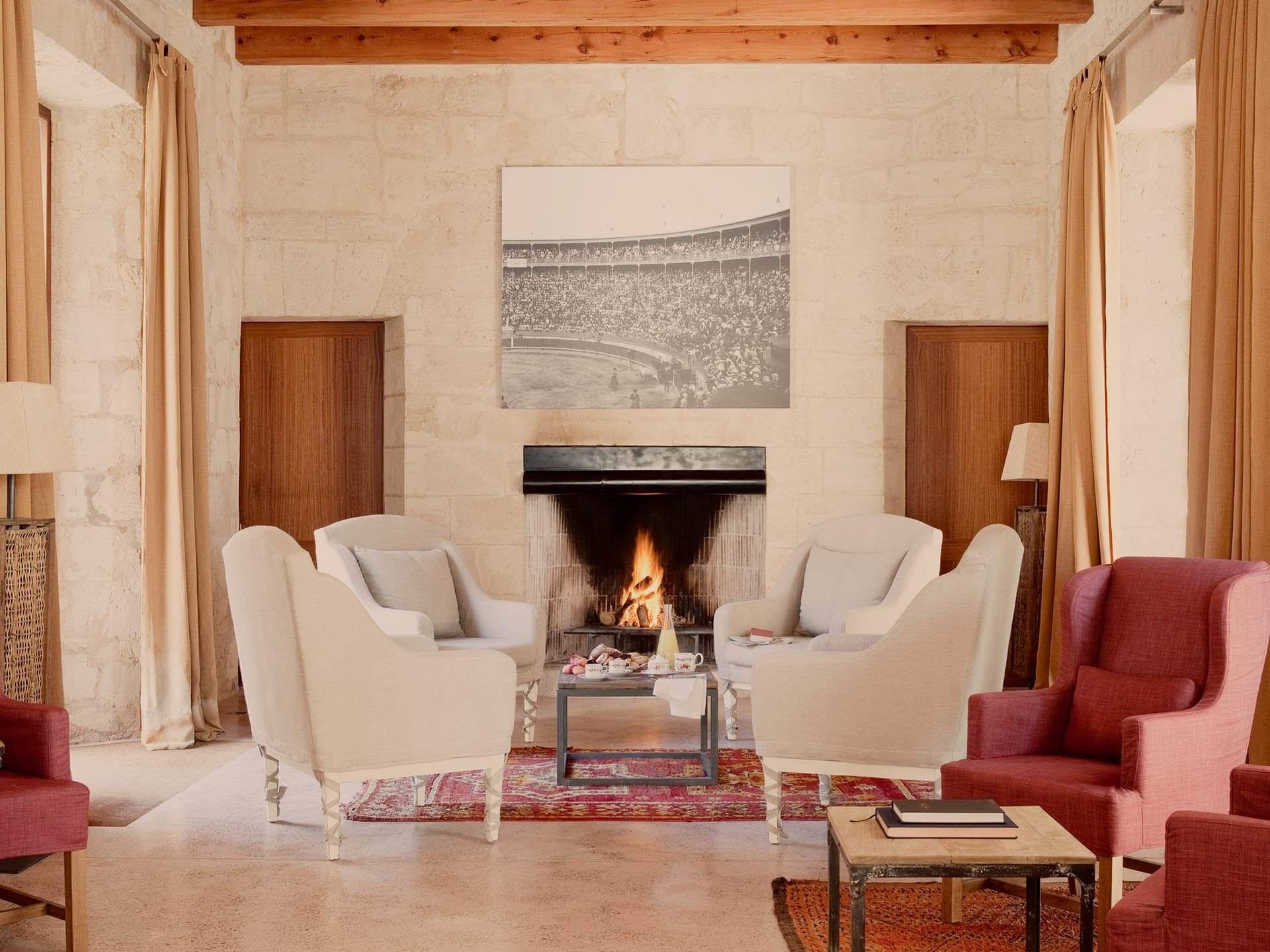 A living room with cream chairs, fireplace, warm wood paneling, and traditional architecture