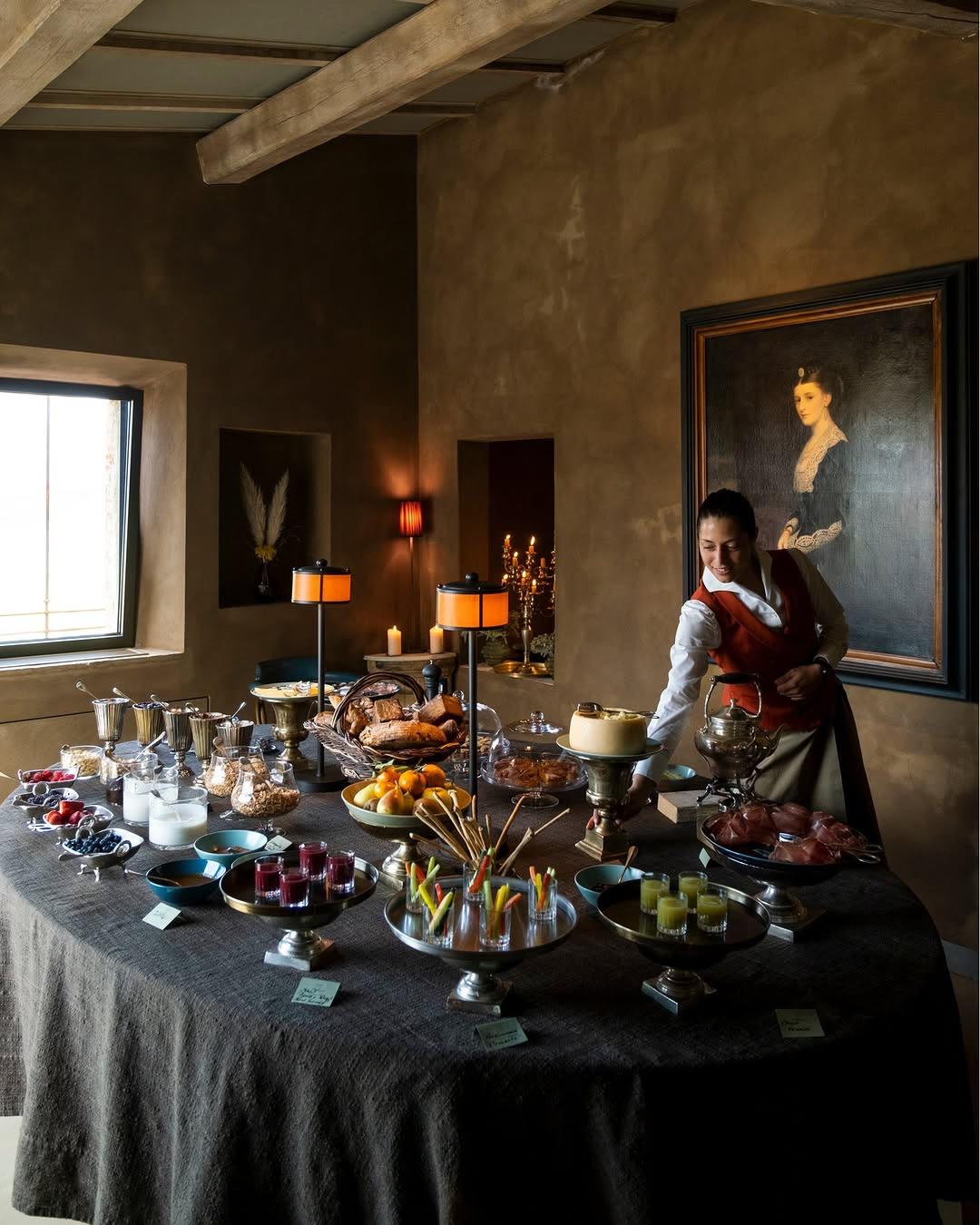 A woman arranging a dessert and appetizer spread on a linen covered table, lit by twin orange lamps
