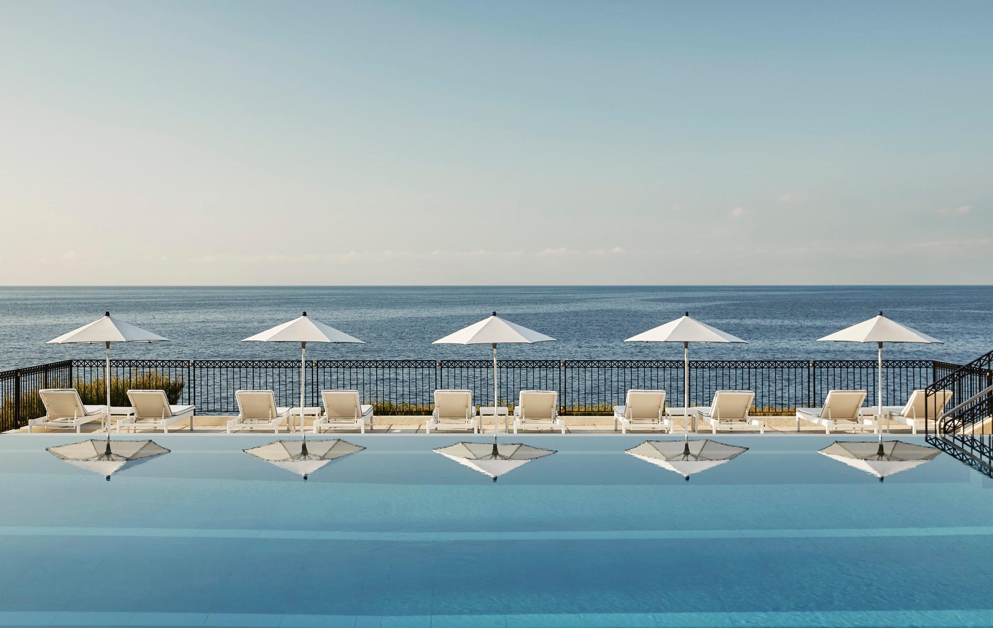 Outdoor pool with beach cabanas lined along calm Mediterranean waters