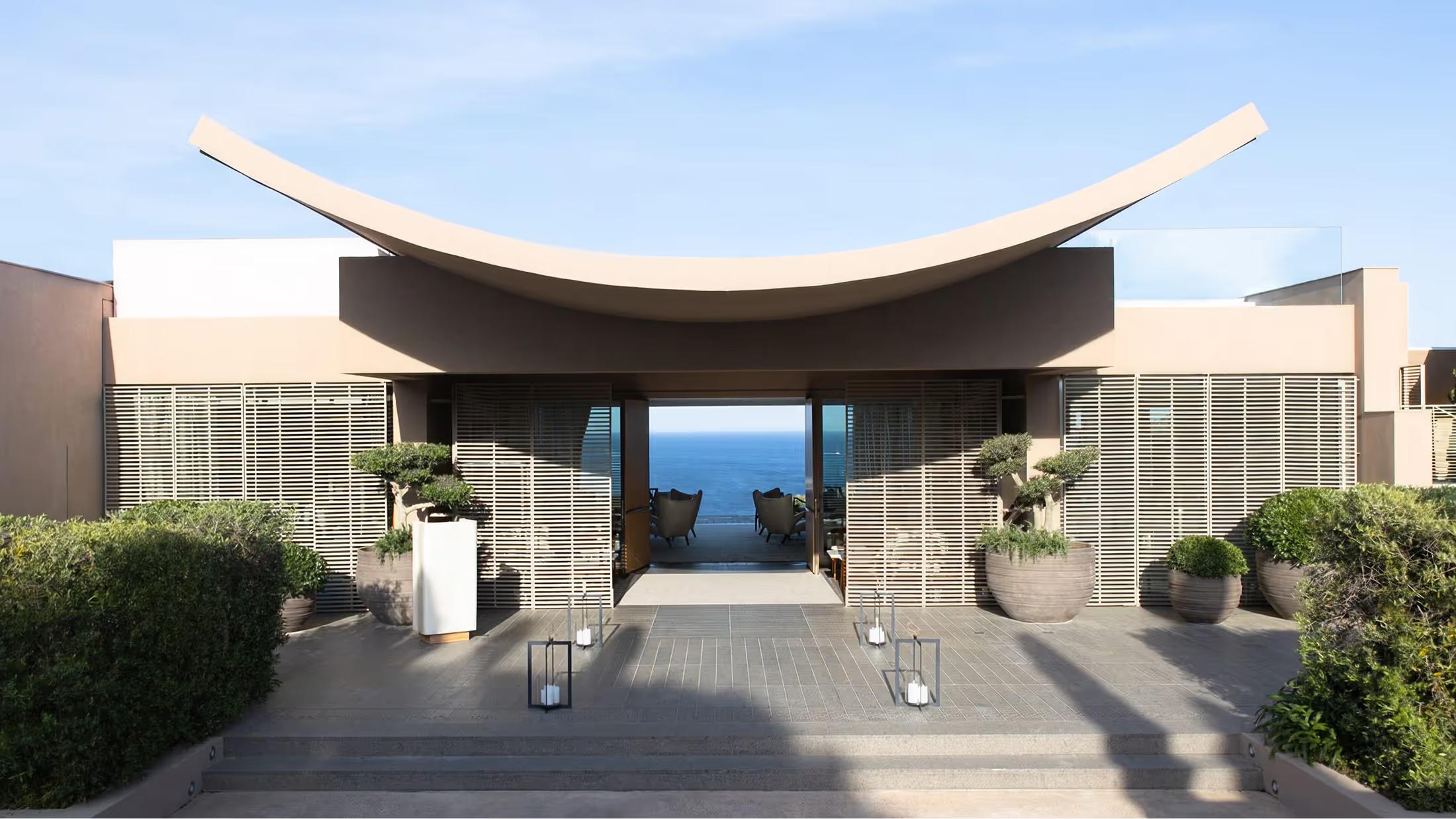 A curved dark pavilion opens onto the Mediterranean Sea and coastline