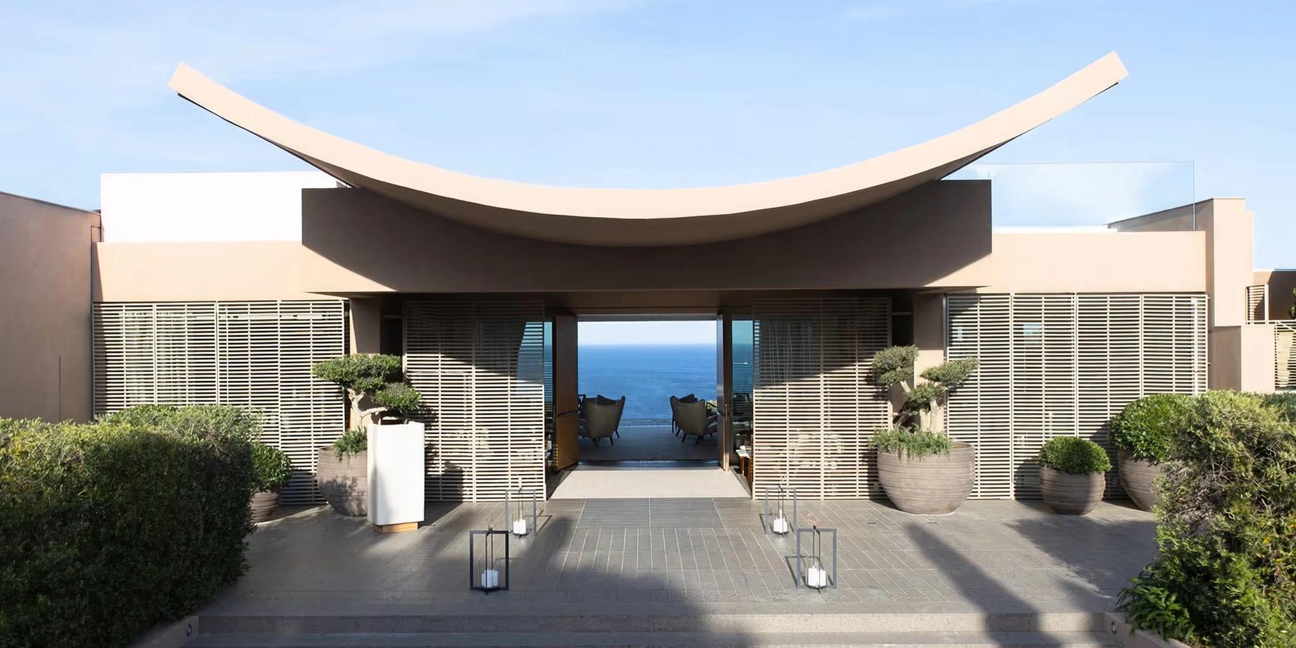 A curved dark pavilion opens onto the Mediterranean Sea and coastline