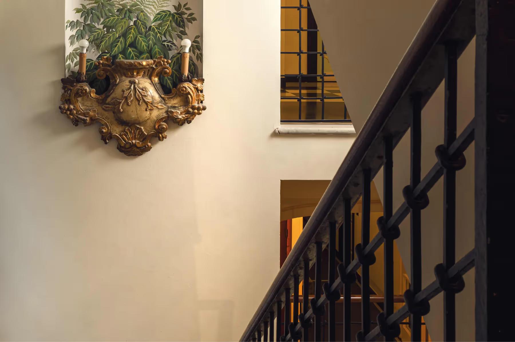 A staircase with iron railing beside climbing ivy on a pale stone wall