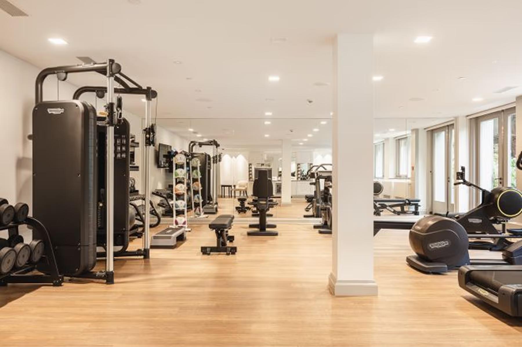 Waldorf Astoria Amsterdam: a gym with workout machines lined against wood-clad walls on light wood flooring in a bright space