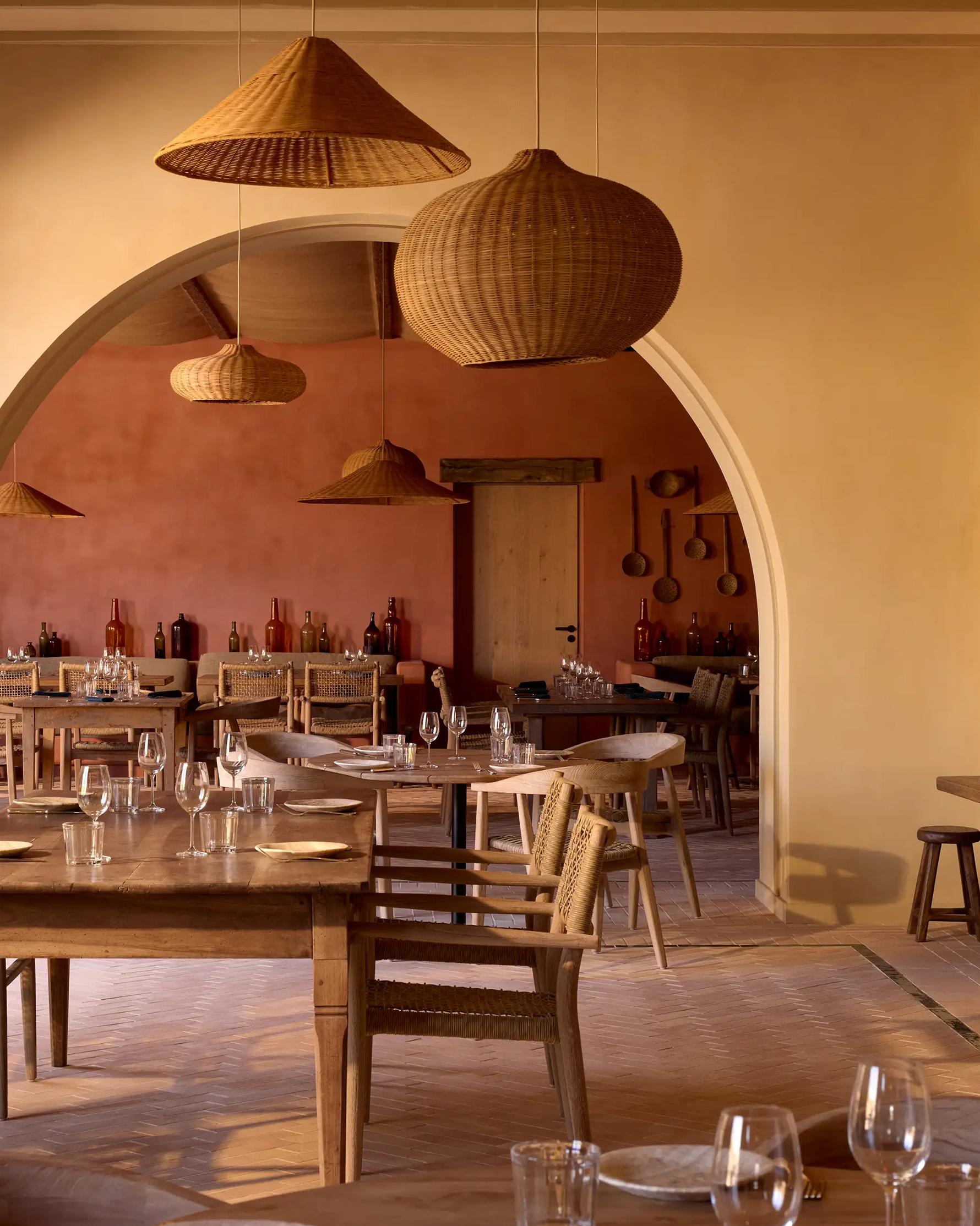 The dining room at Nonna Bazaar seen through a wide arch, with wicker pendant lamps and wooden tables