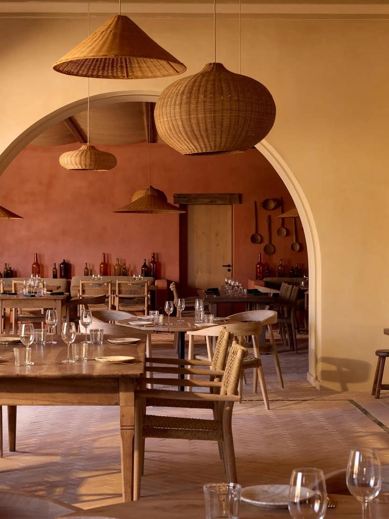 The dining room at Nonna Bazaar seen through a wide arch, with wicker pendant lamps and wooden tables
