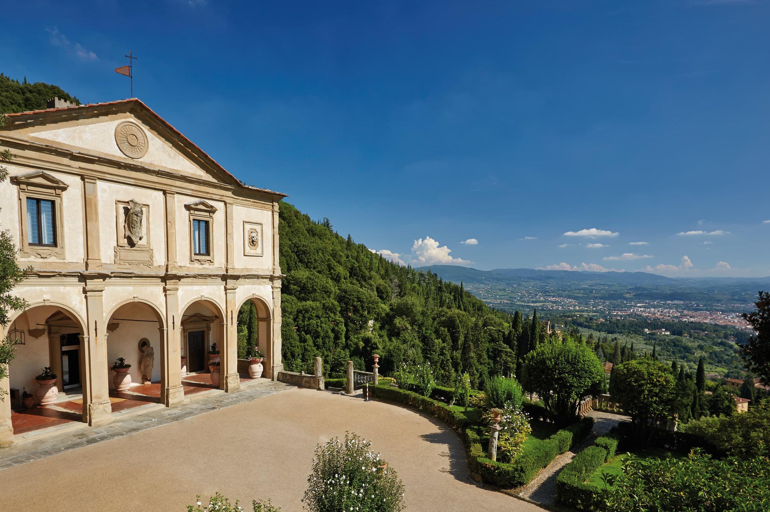 Villa San Michele: cream building with arched loggia, stone ornaments, and panoramic view of the Florence valley beyond cypress