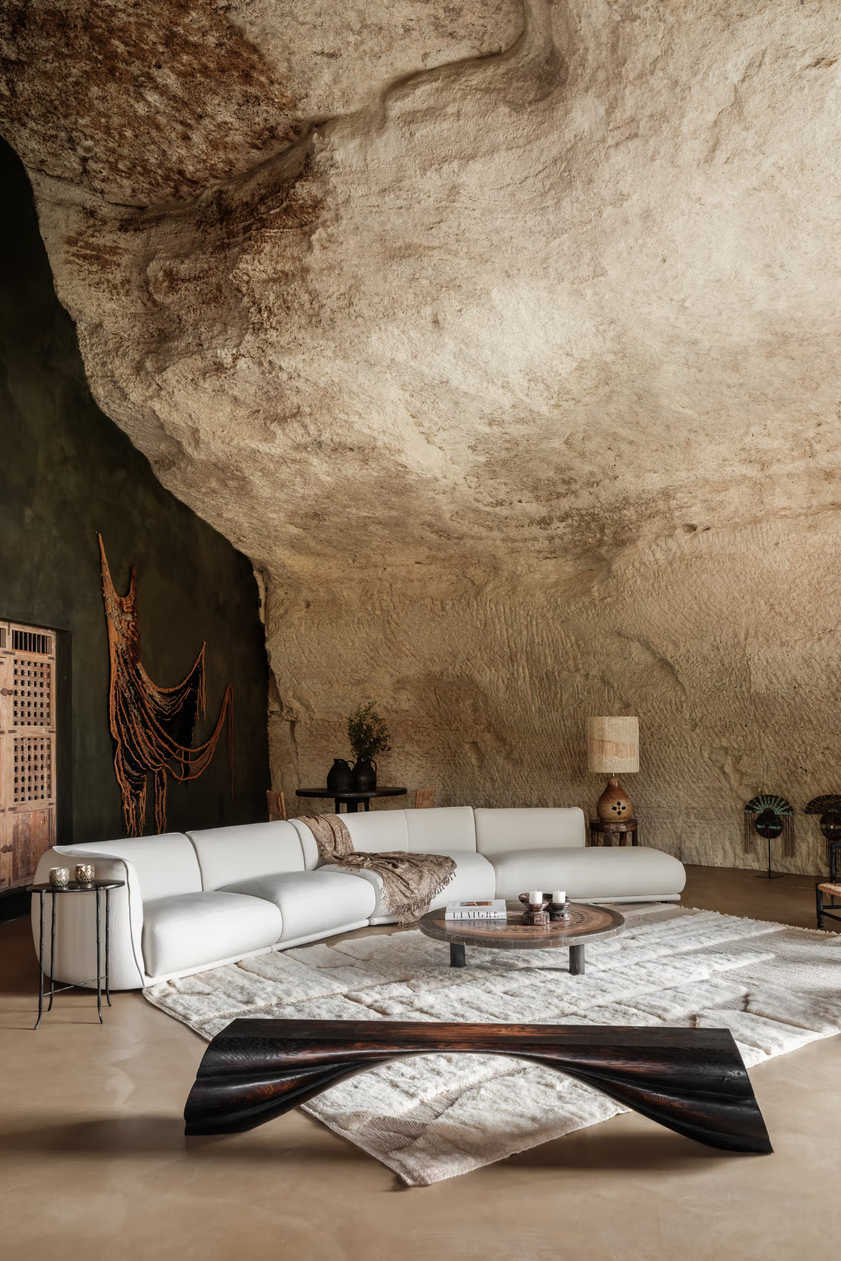 La Bergerie: cavernous living room carved into stone with monumental raw limestone wall, curved cream seating, arched opening
