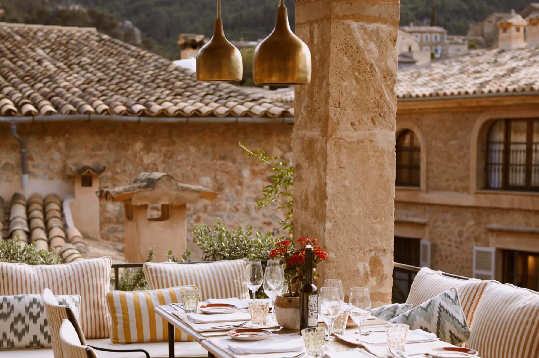 Courtyard dining area with natural stone walls, hanging pendant lights, and rustic wooden furnishings