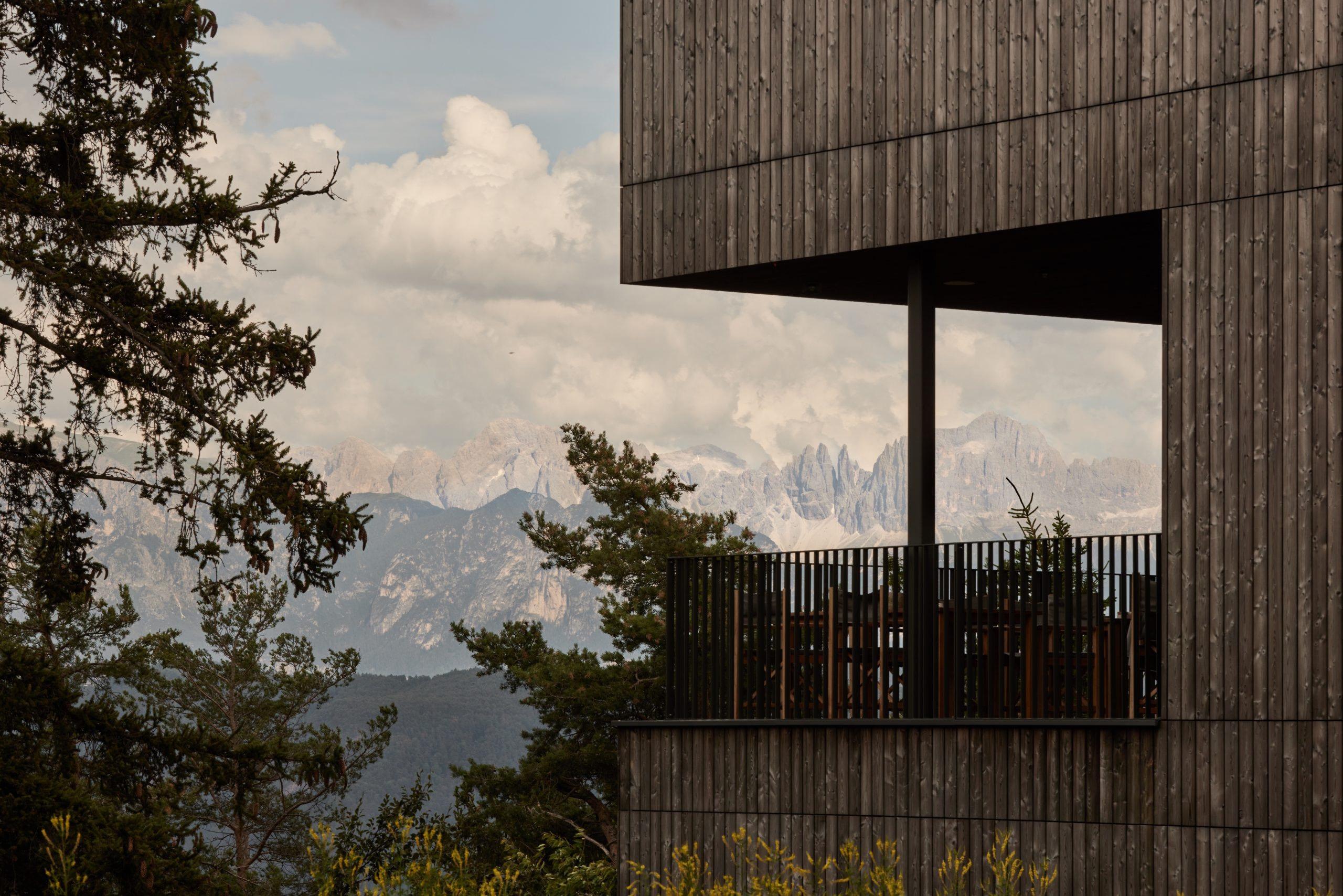 Hotel Saltus: cantilevered wooden balcony overlooking Dolomite mountain peaks under dramatic sky