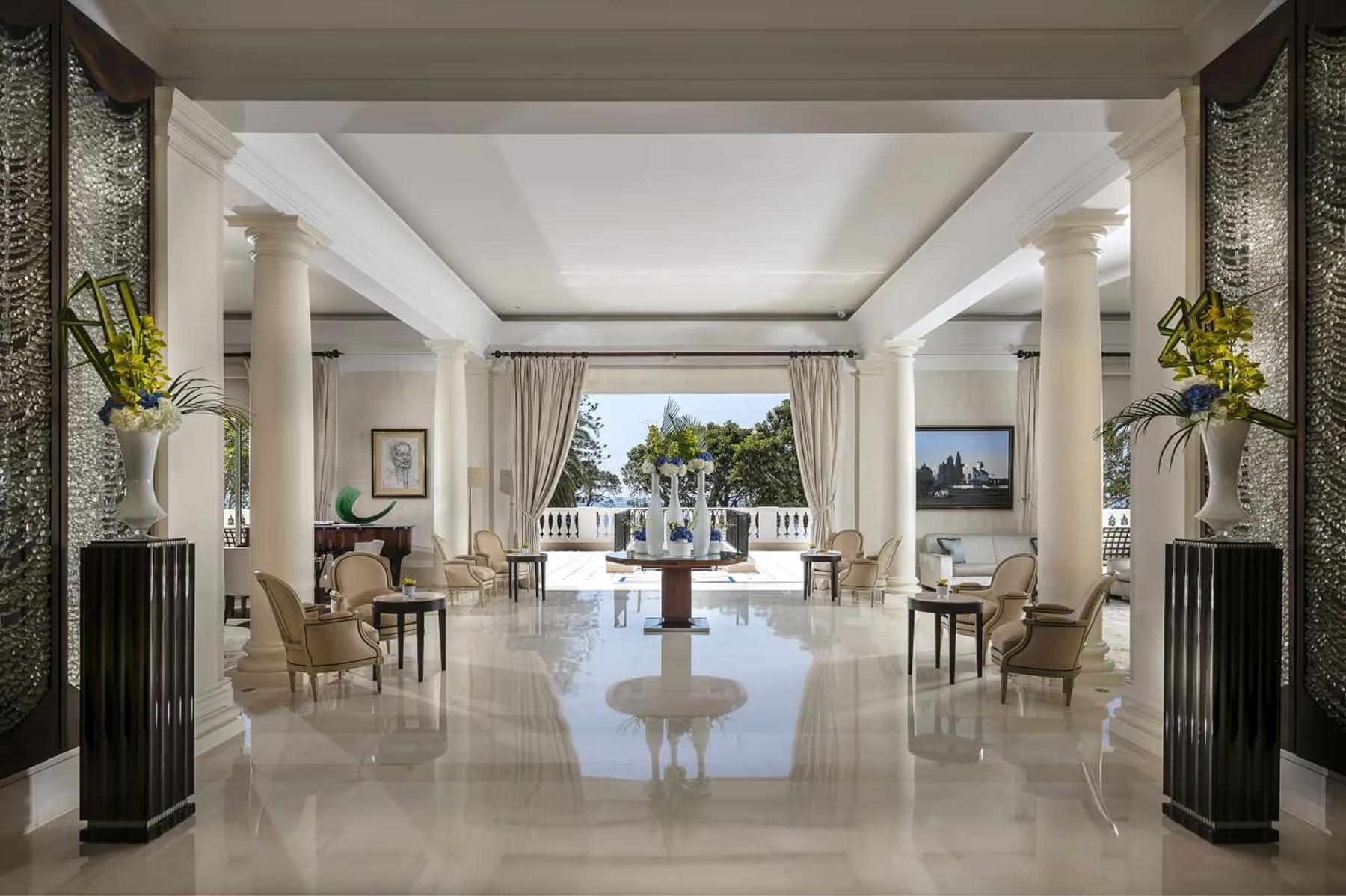 A grand hall with columns, polished floors, and sea views through open doors