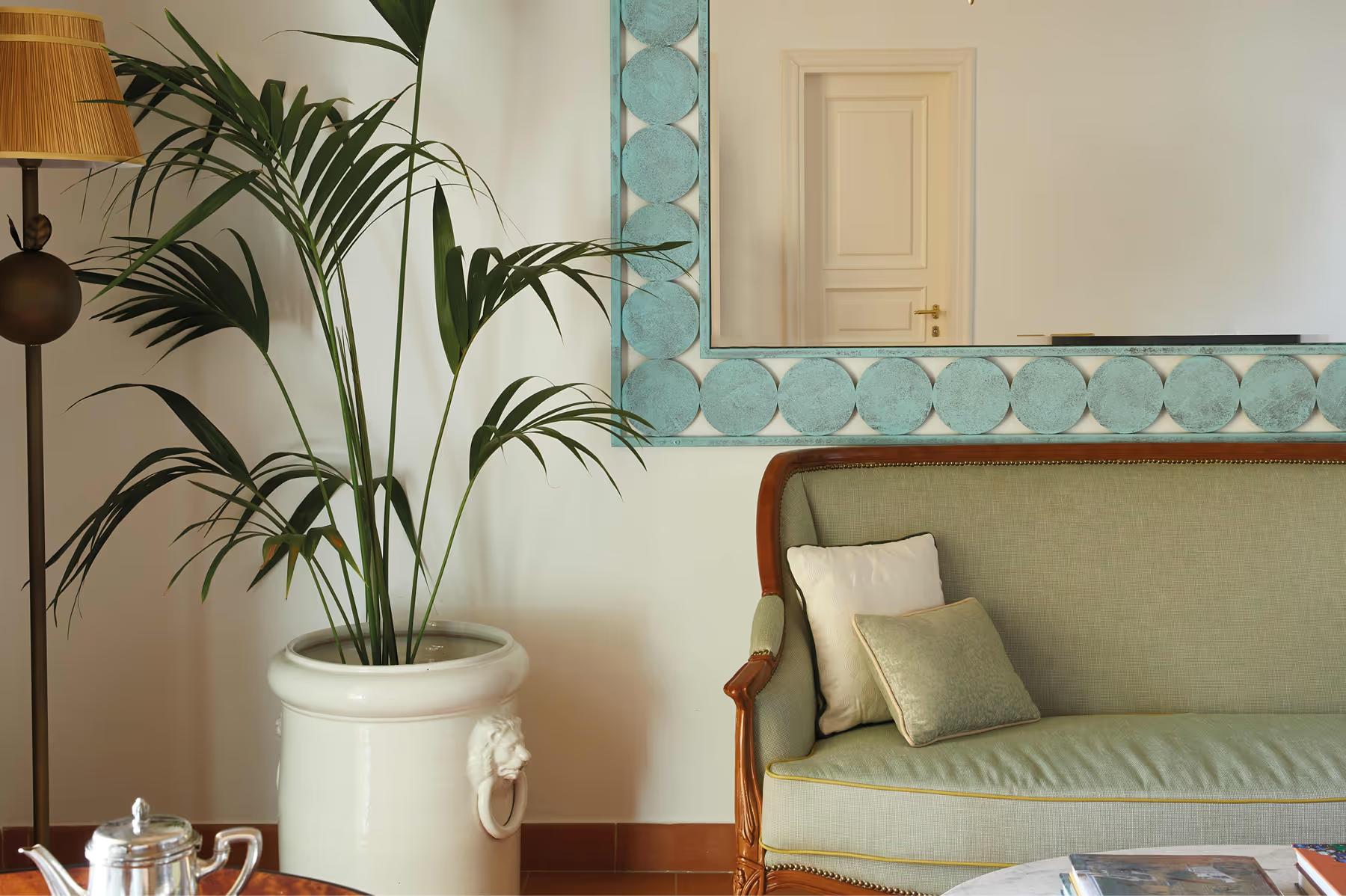 Caruso: living area with pattern-accented walls, potted palm plant, cream furnishings, and contemporary art
