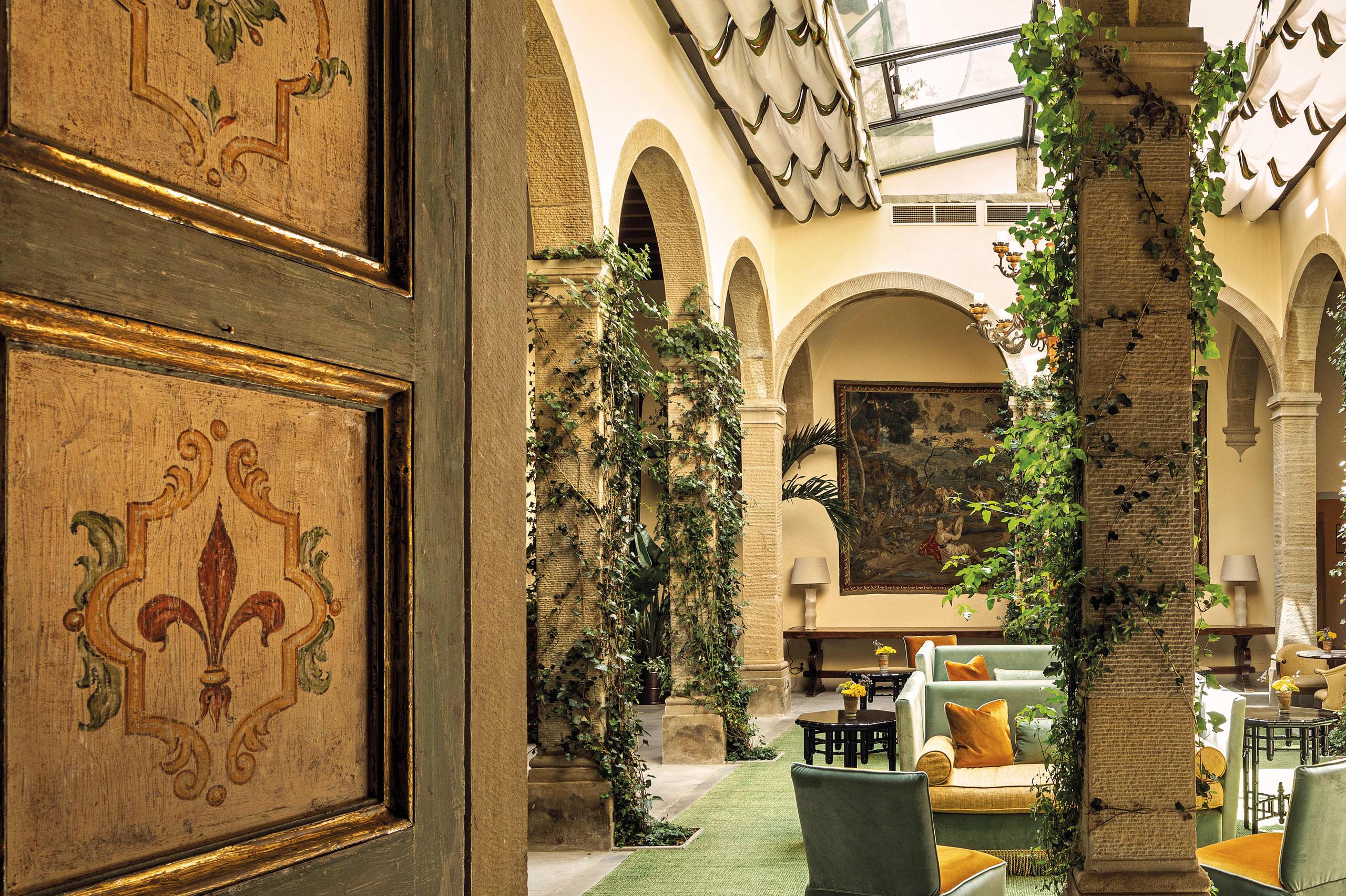 Villa San Michele: vaulted courtyard with decorated wooden doors, climbing ivy, arched columns, and green seating with gold accents