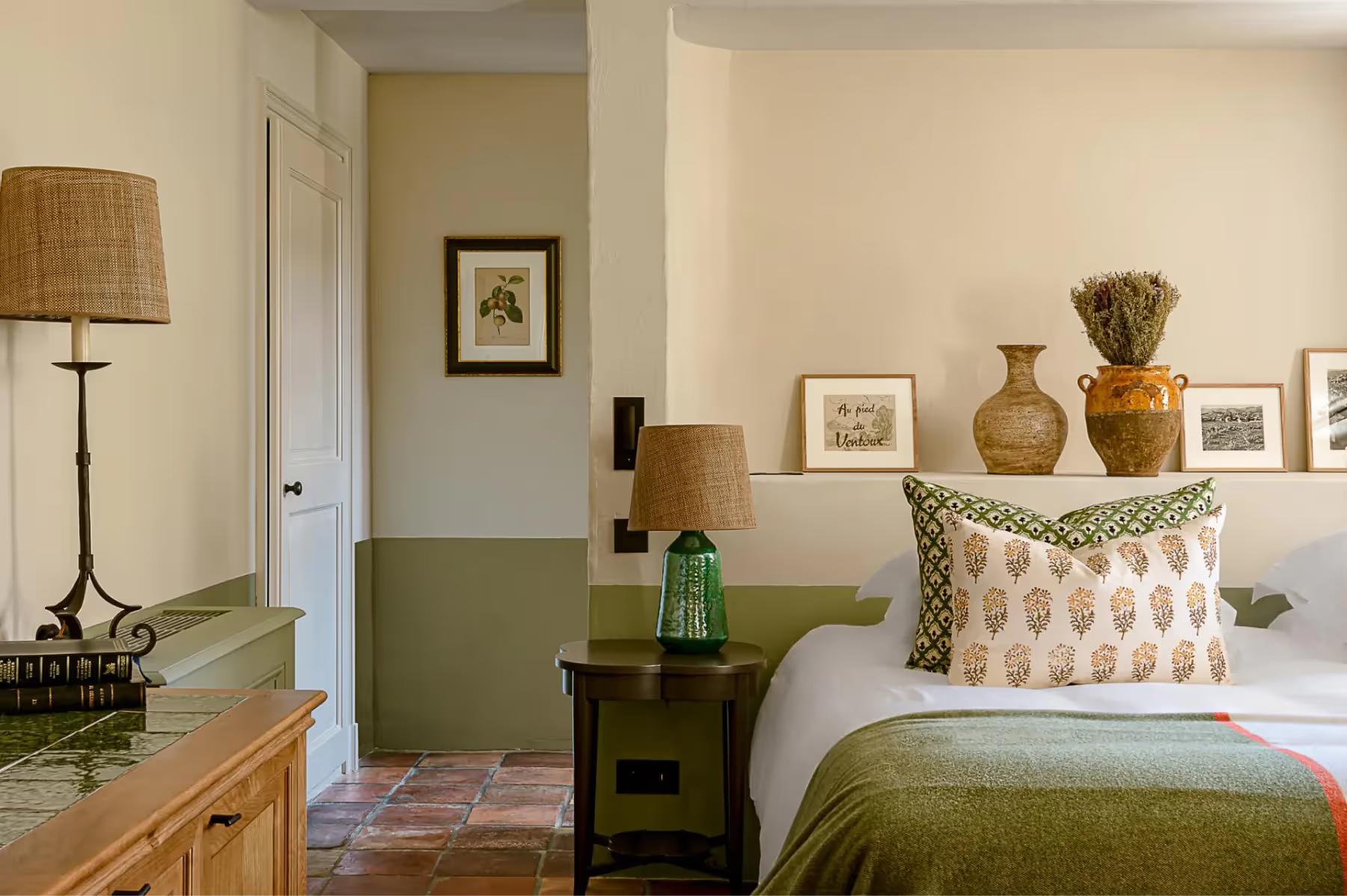 A bedroom with green wall panels, ceramic accents, a bed with patterned headboard, and warm wood tones