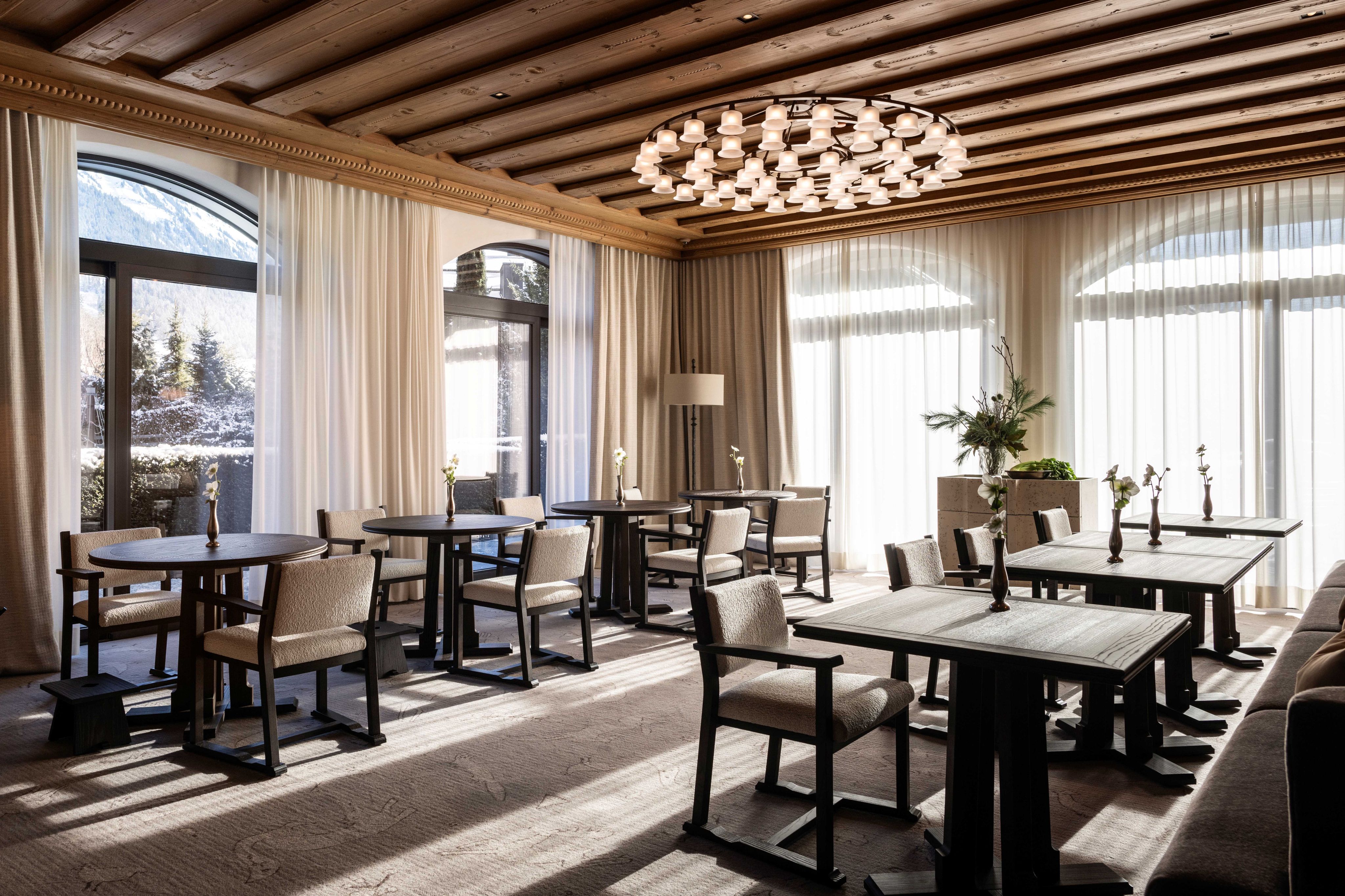 A timber-ceilinged dining room with round tables and armchairs in Gstaad
