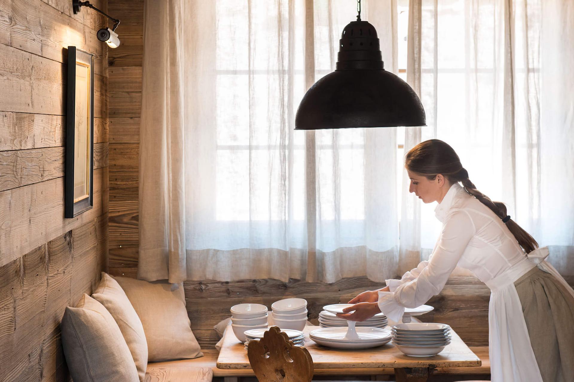 Staff member plating food in a bright dining room beneath black pendant light