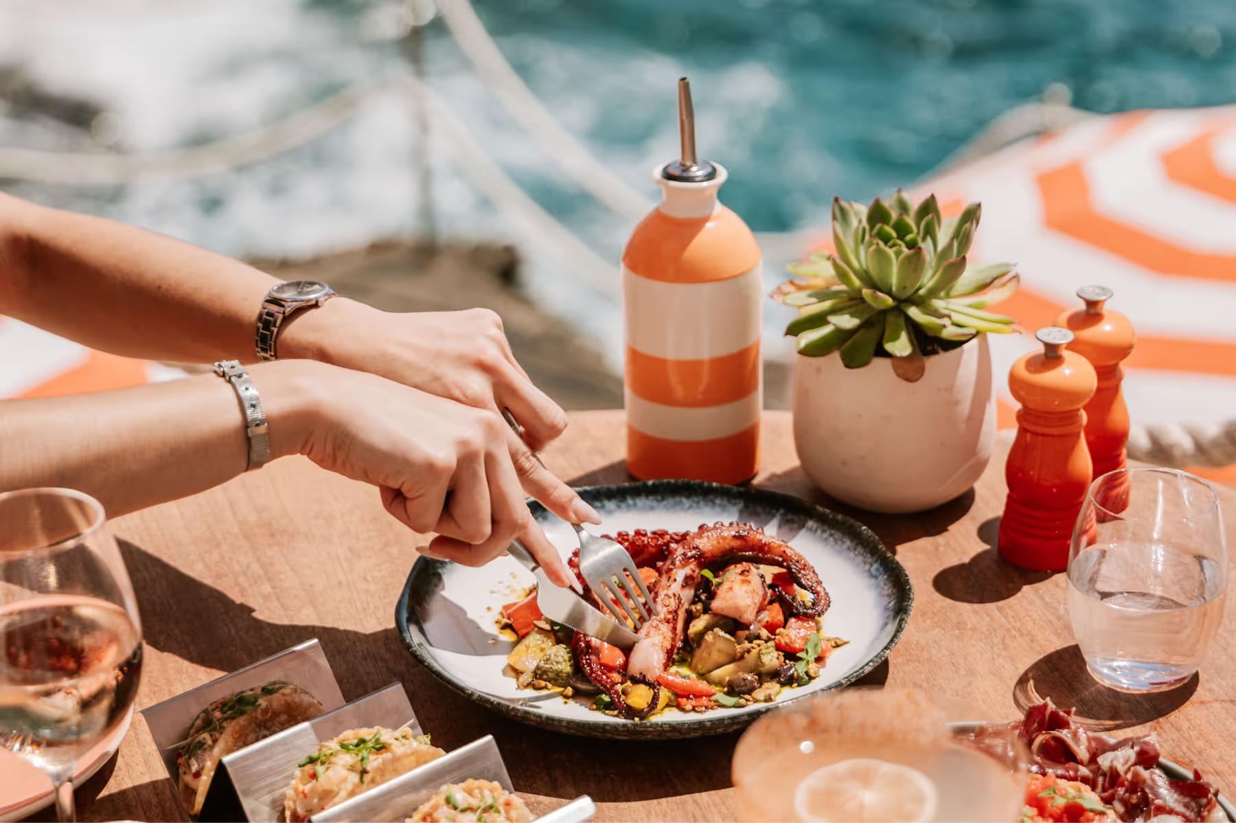 Poolside dining with orange umbrellas and sea backdrop