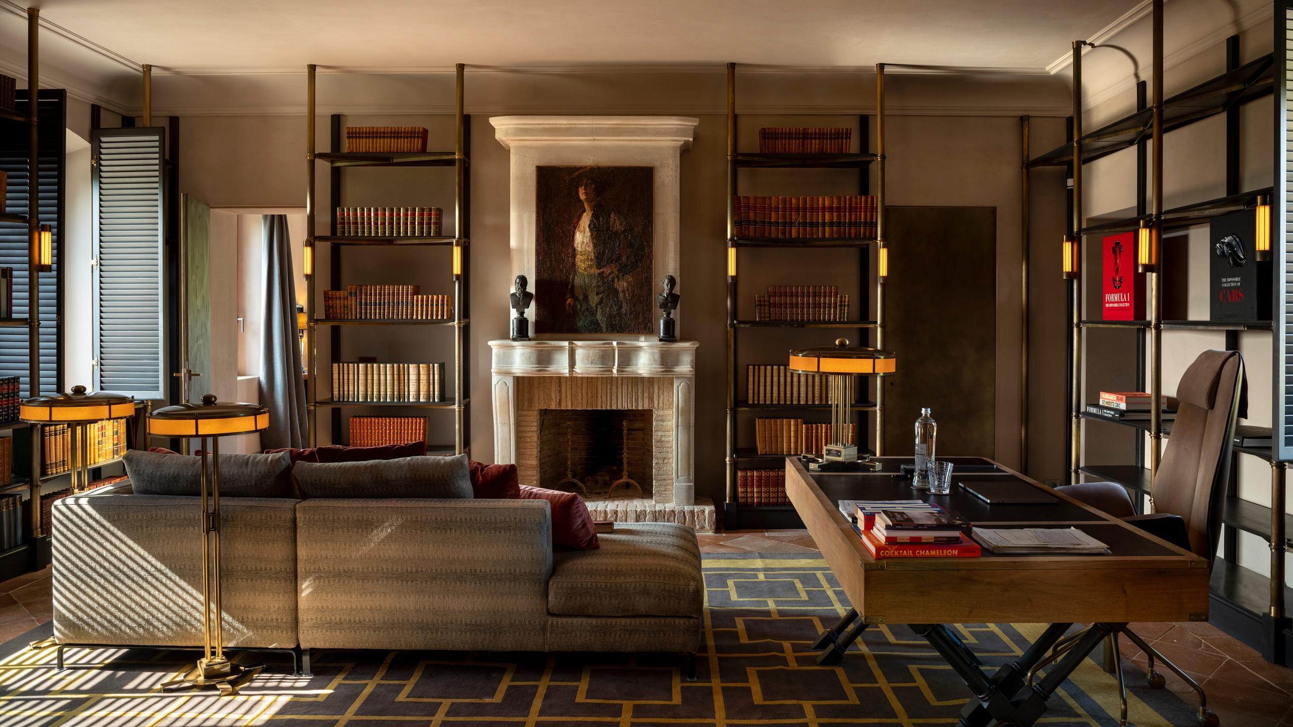 Castello di Reschio: a library lounge with a stone fireplace, ladder shelving, and leather sofas around a brass legged table