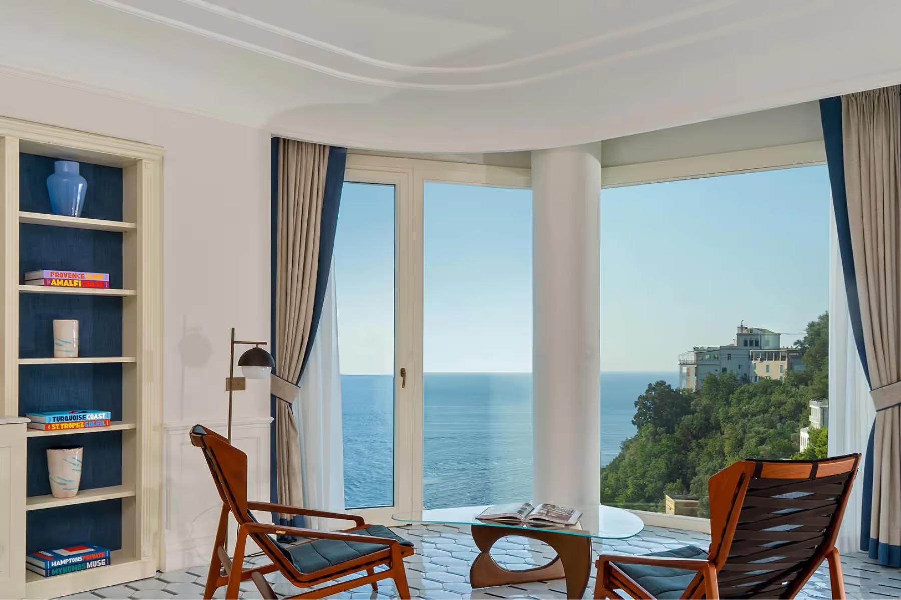 Borgo Santandrea: suite with curved bay windows framing sea views, modern furnishings, and blue-toned decor
