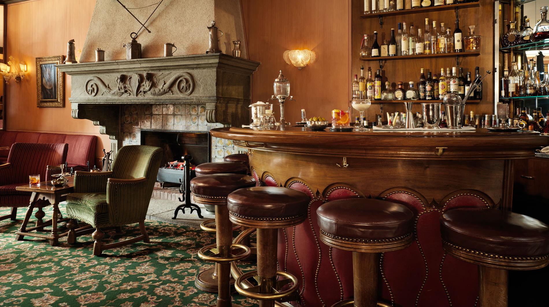 Badrutt’s Palace Hotel: bar lounge with wood paneling, fireplace, and seated guests in warm lighting