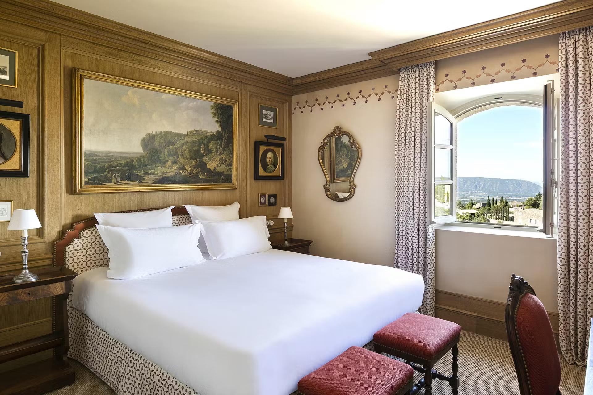 Bedroom with pale yellow walls, white bedding, red accent pillows, and valley views
