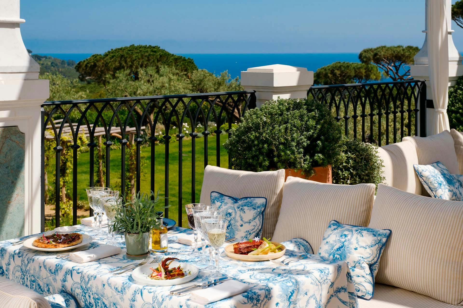 Covered terrace overlooking sea and forest with dining setup and blue-patterned cushions