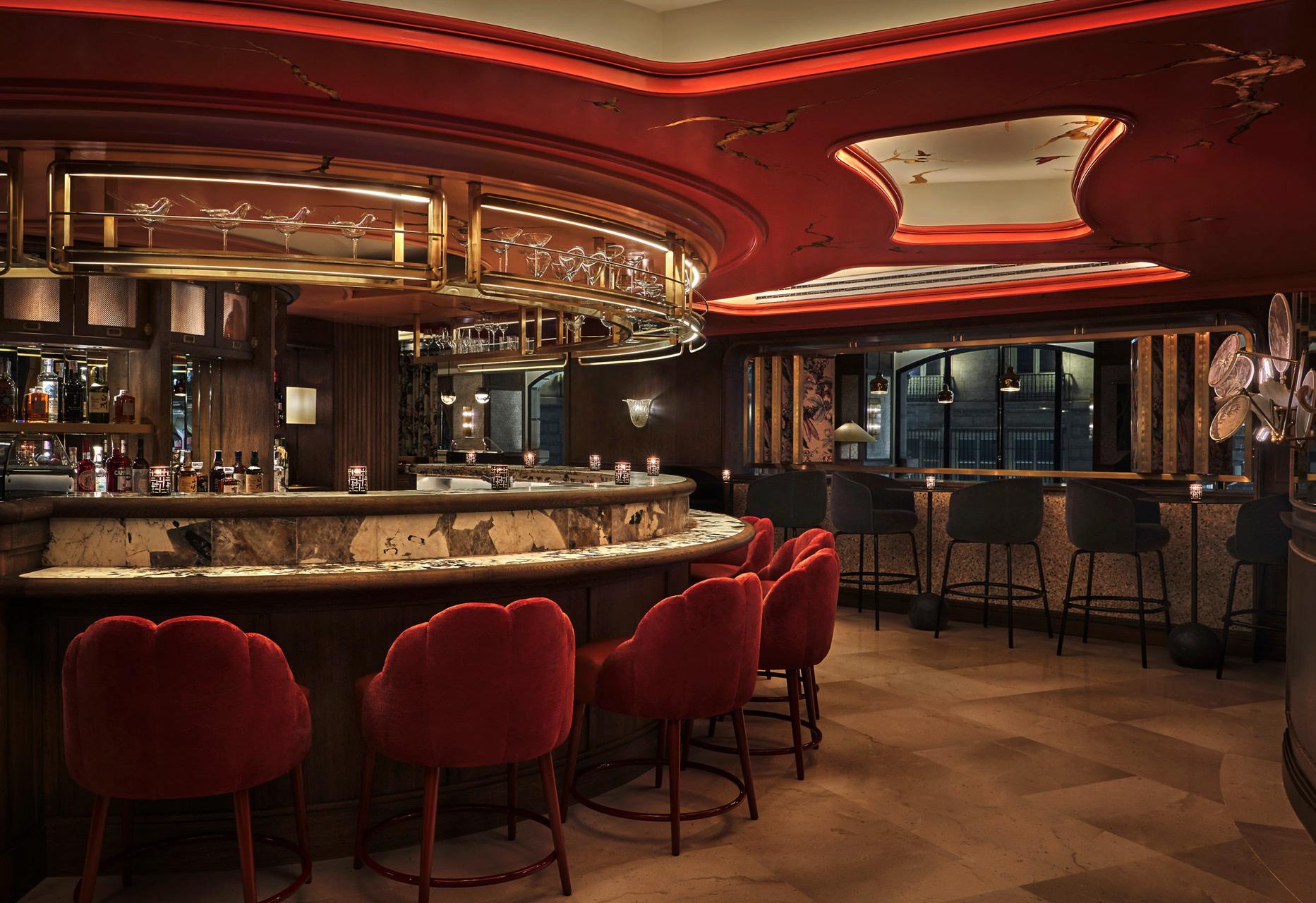 Four Seasons Hotel Madrid: cocktail bar with deep red upholstered seating, dark wood paneling, brass accents, and amber lighting