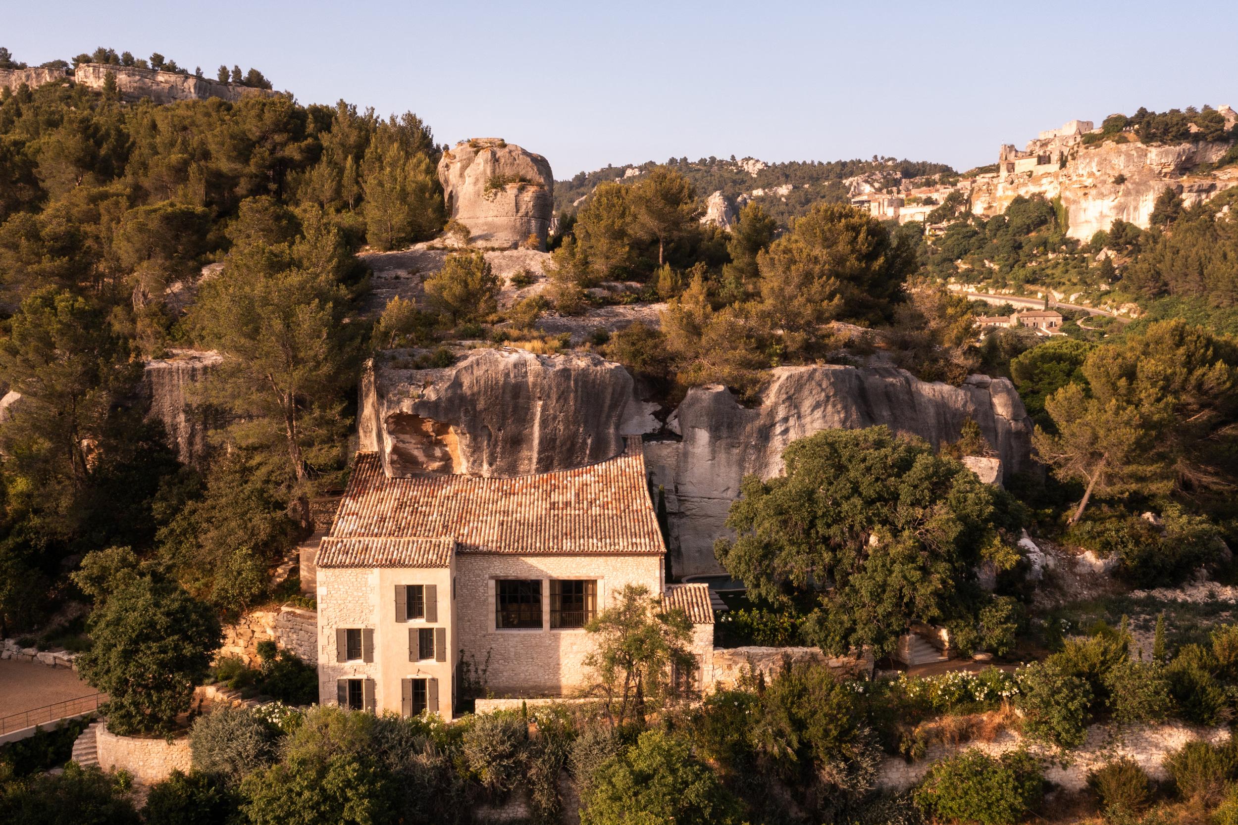 La Bergerie: aerial view of terra-cotta-roofed villa complex carved among limestone formations, cypress, forested valley