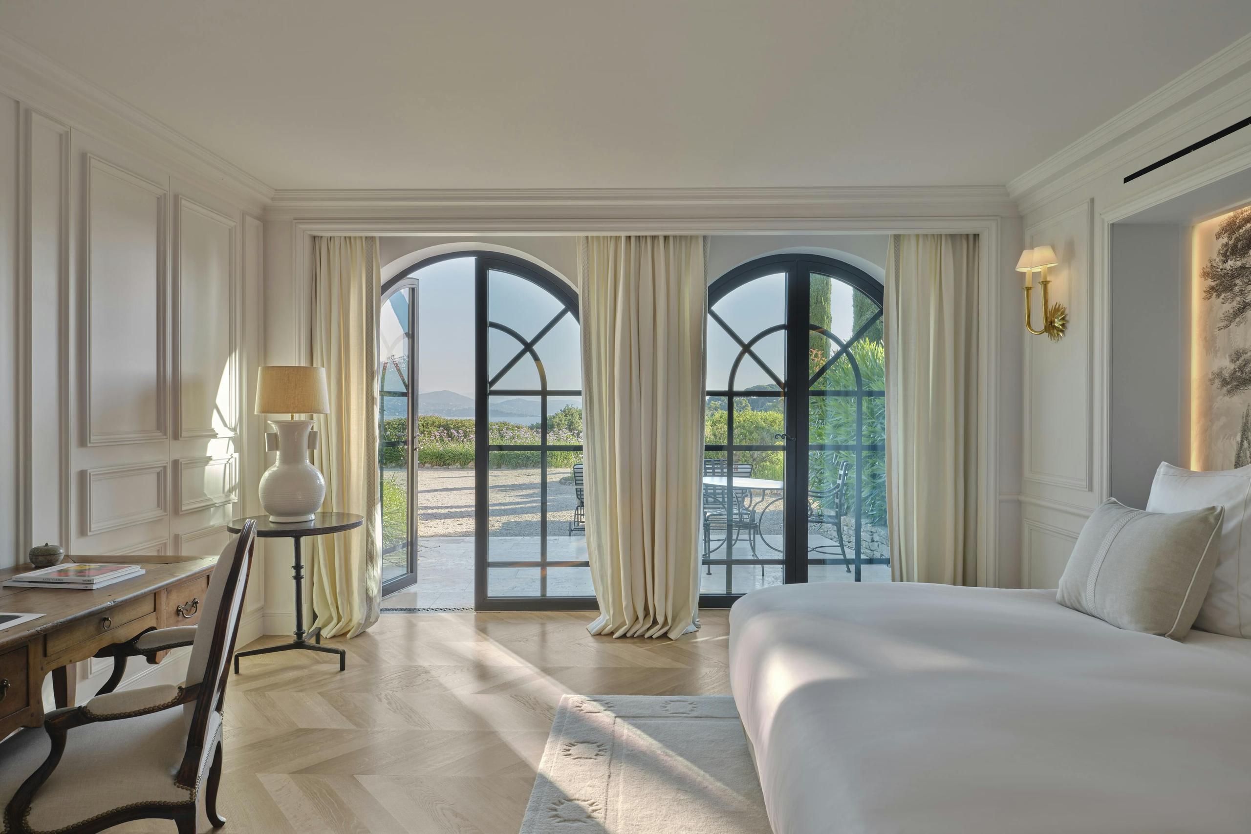 Bright bedroom with white furnishings, tall doors opening onto a bay-view terrace