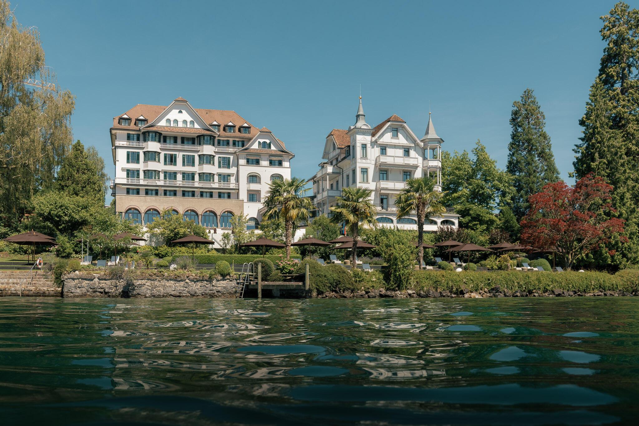Hotel building complex seen from Lake Lucerne waterside, green grounds and manicured landscaping