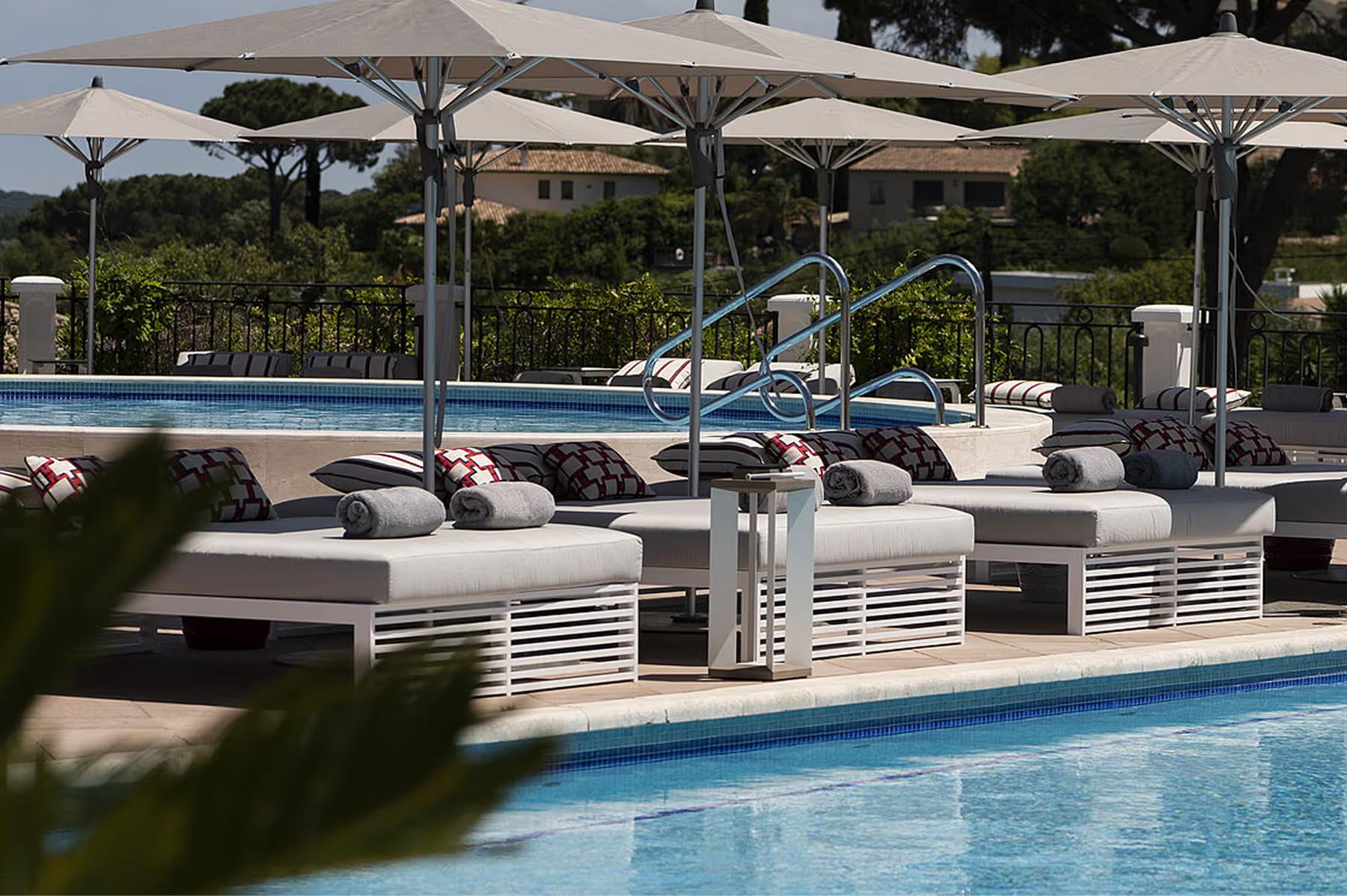 Shaded pool area with tan loungers and umbrellas on manicured grounds