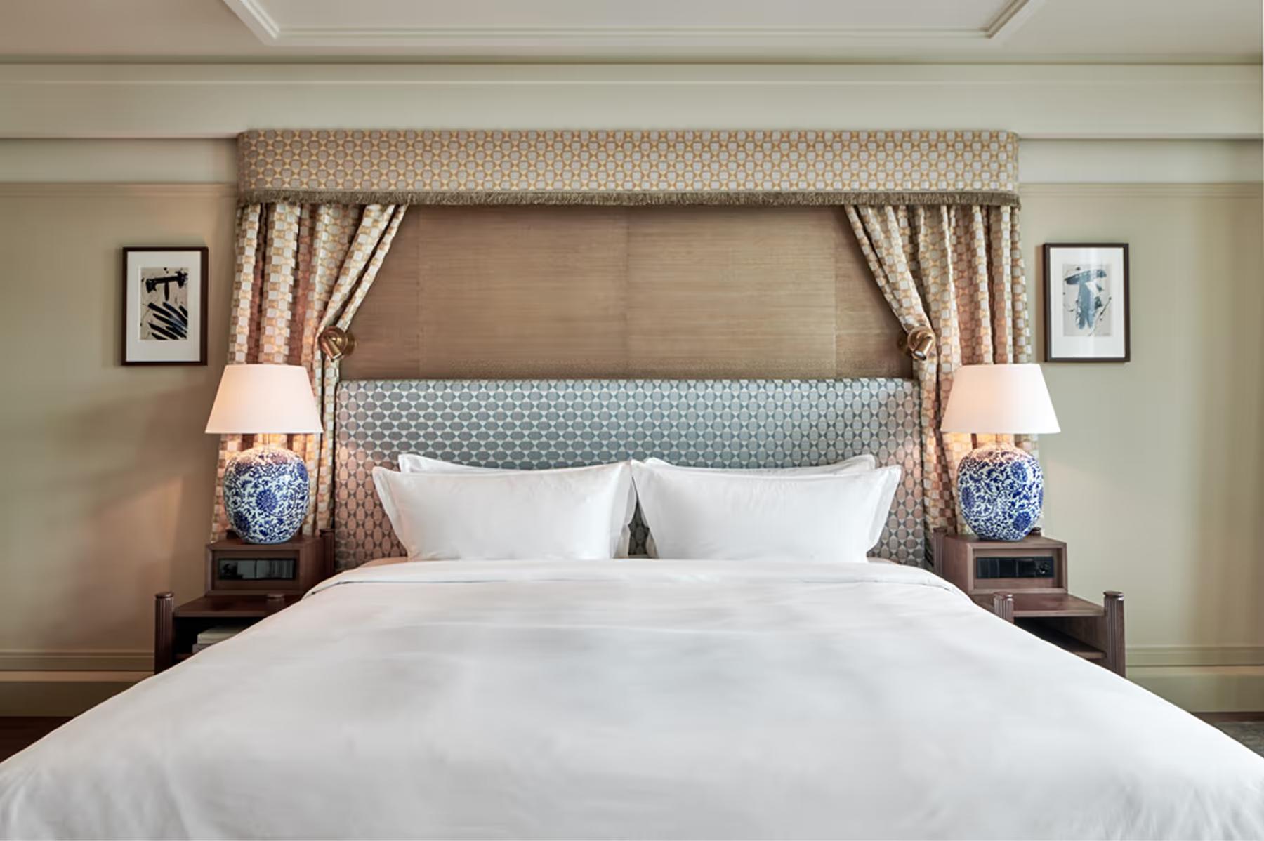 Bedroom with upholstered headboard, cream bedding, and patterned window curtains