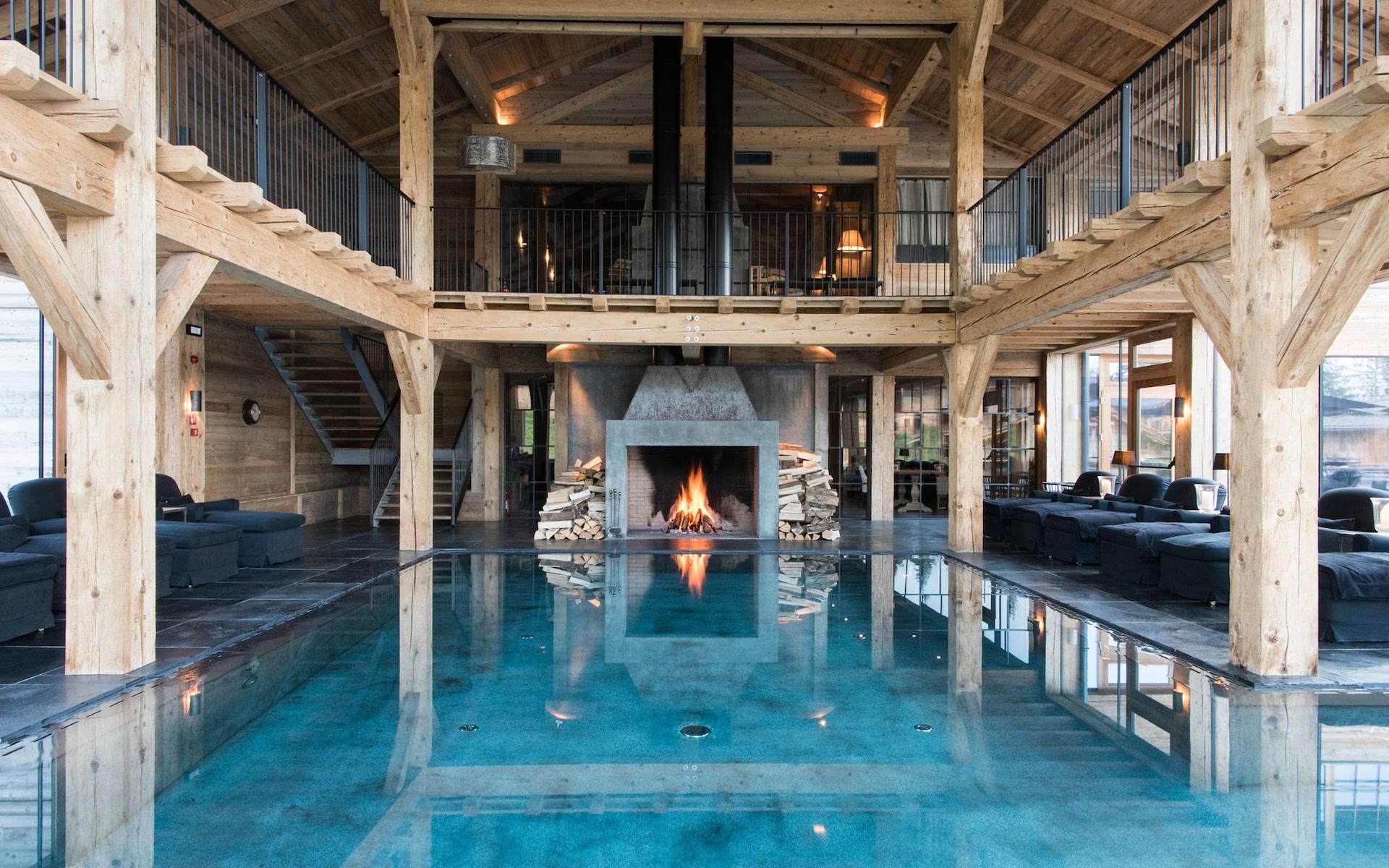 Indoor pool with fireplace, wooden beams, and surrounding windows