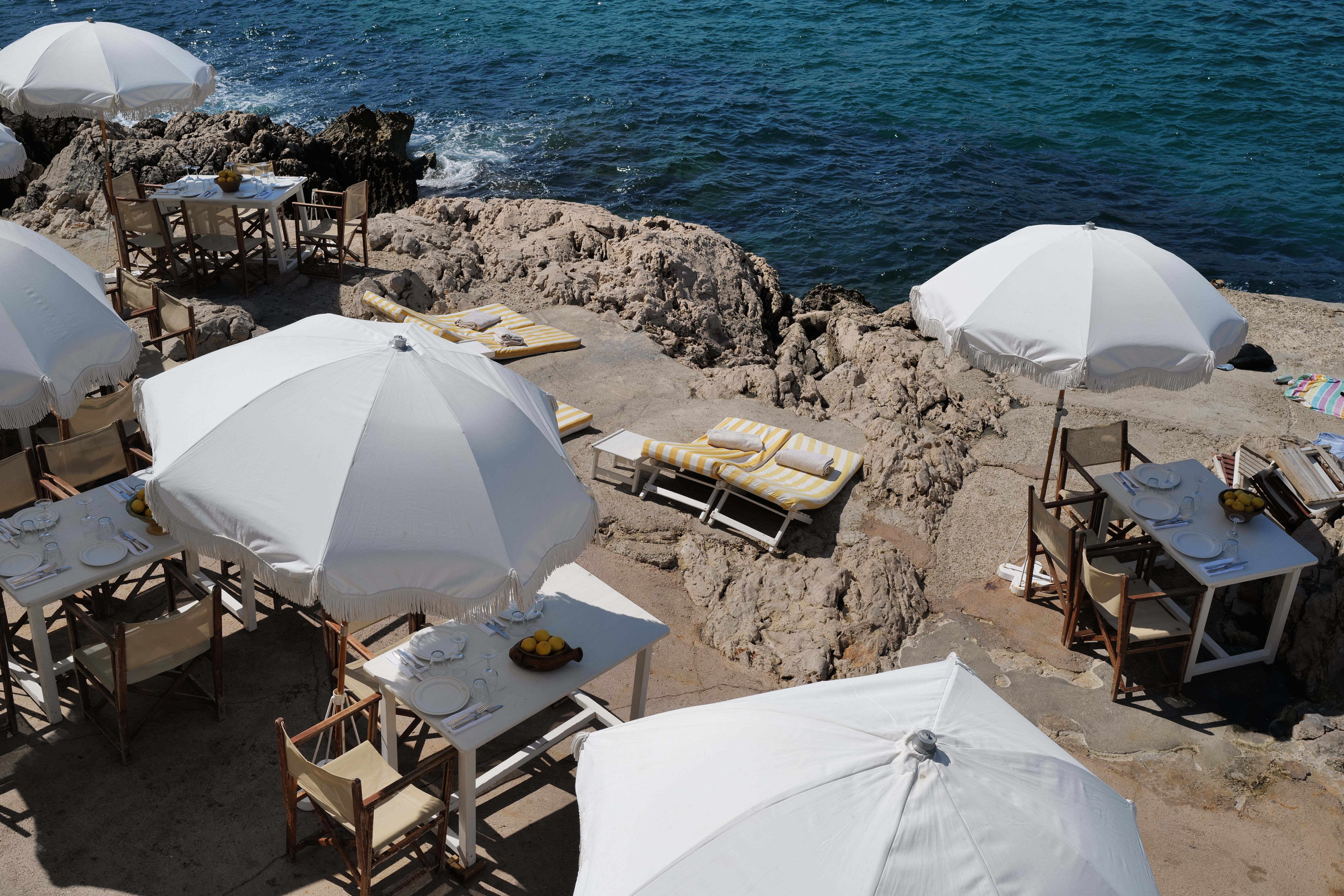 A set table under a fringed parasol at Tuba Club, the rocks and open sea beyond