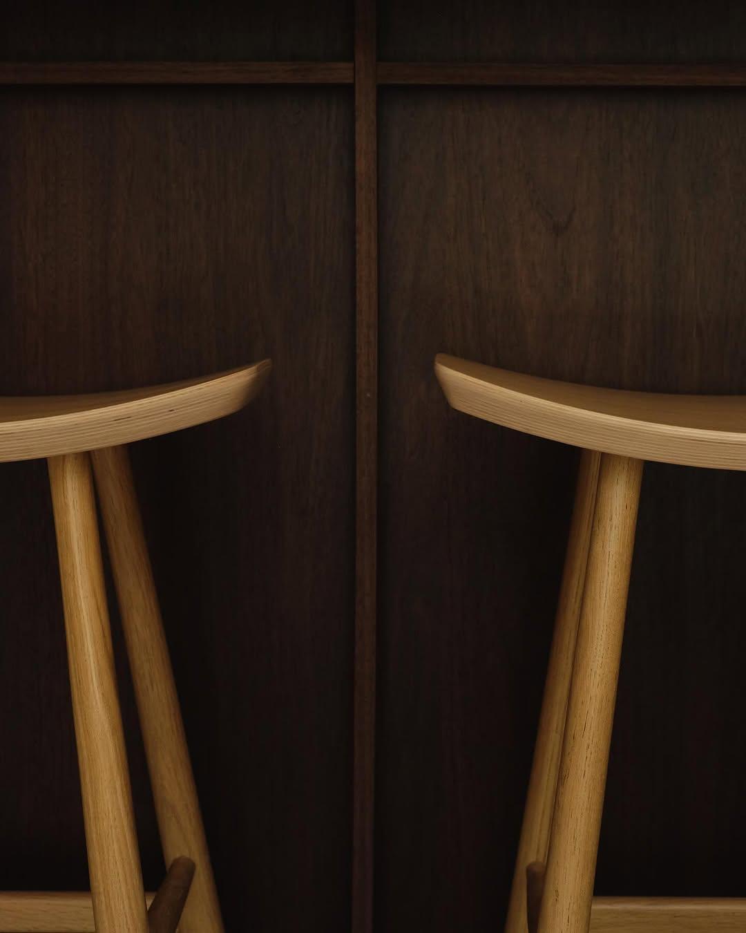 Two light-wood stools against the walnut paneling at Haku
