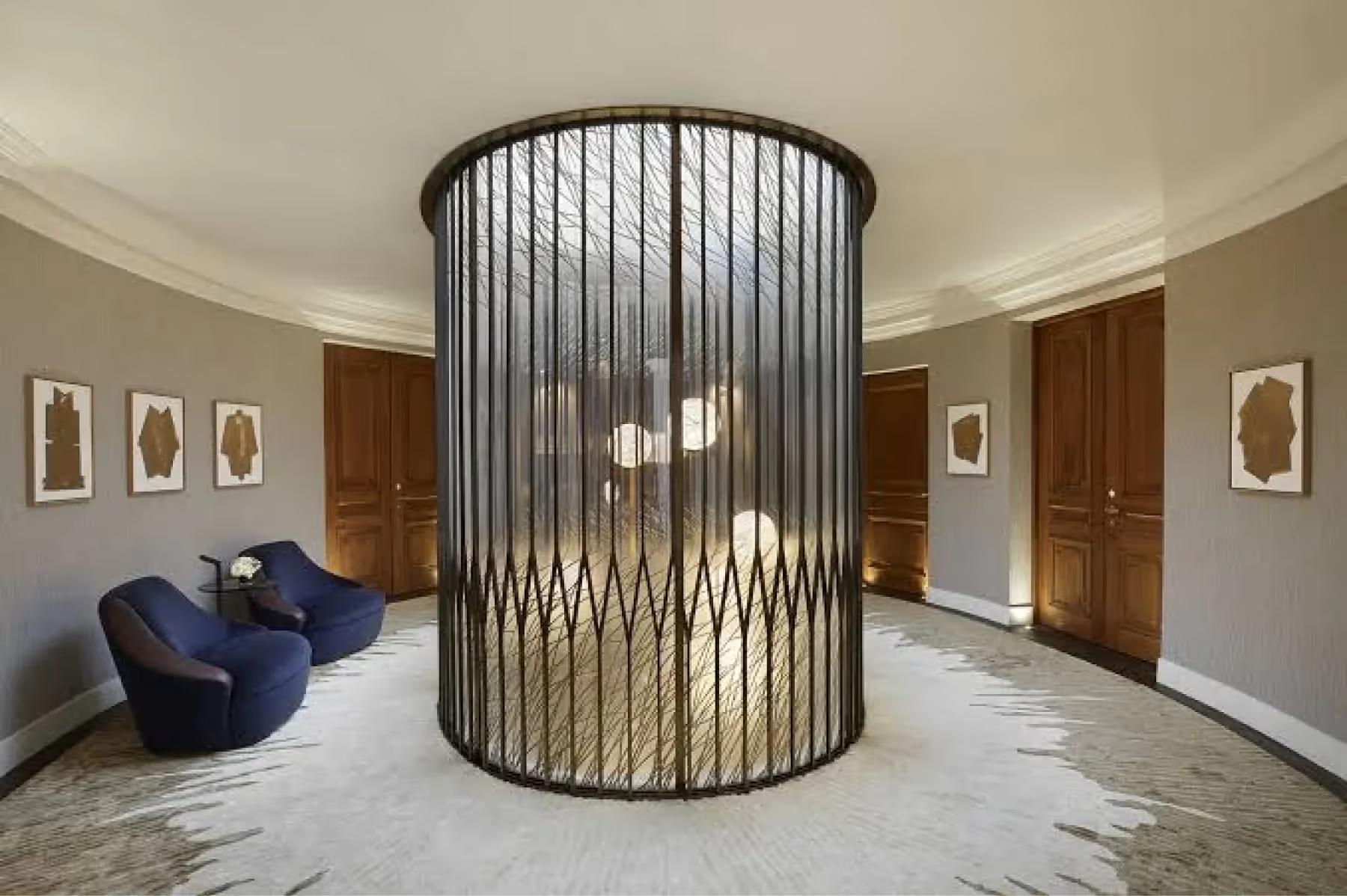 Maison Villeroy: a curved cylindrical black metal sculpture in a foyer with blue armchair and cream walls