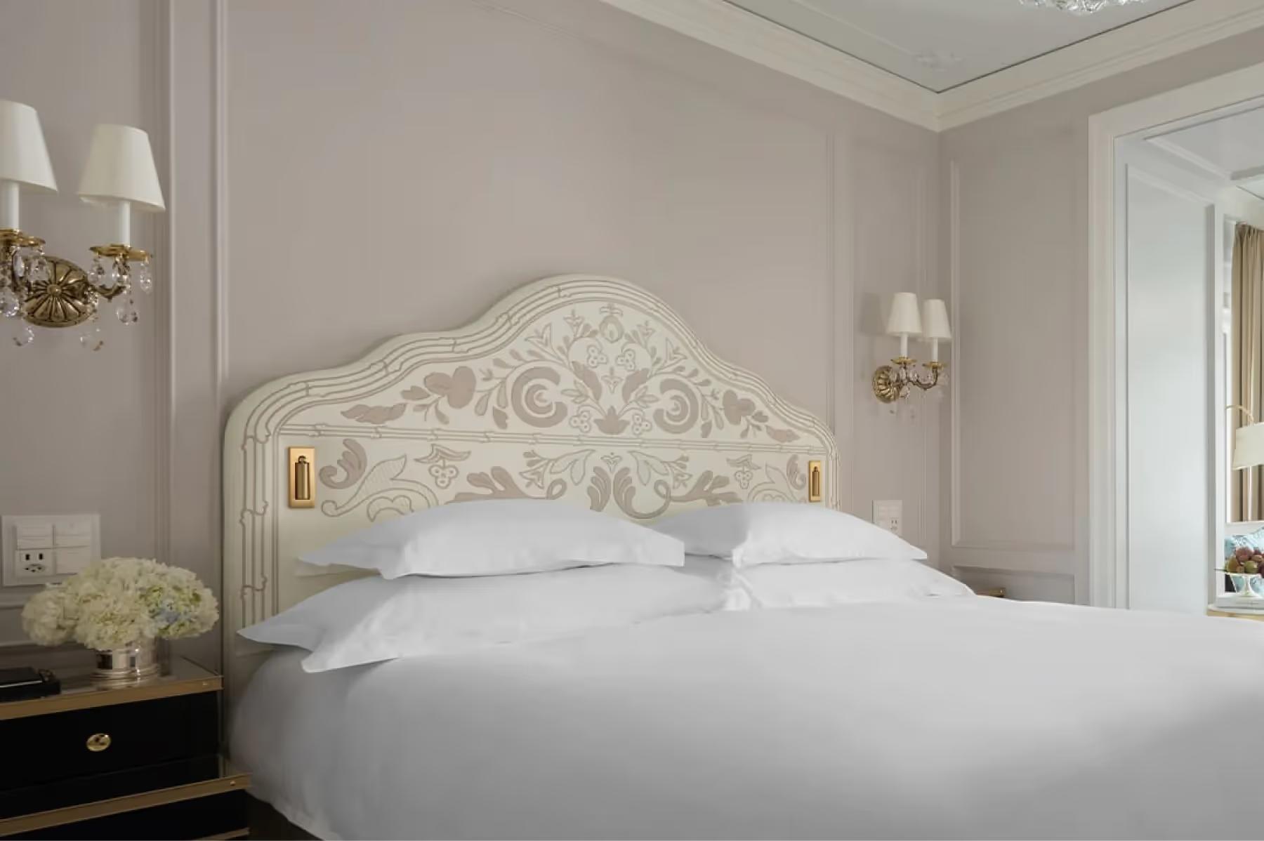 Badrutt’s Palace Hotel: bedroom with ornate headboard, white bedding, and classic wall sconces