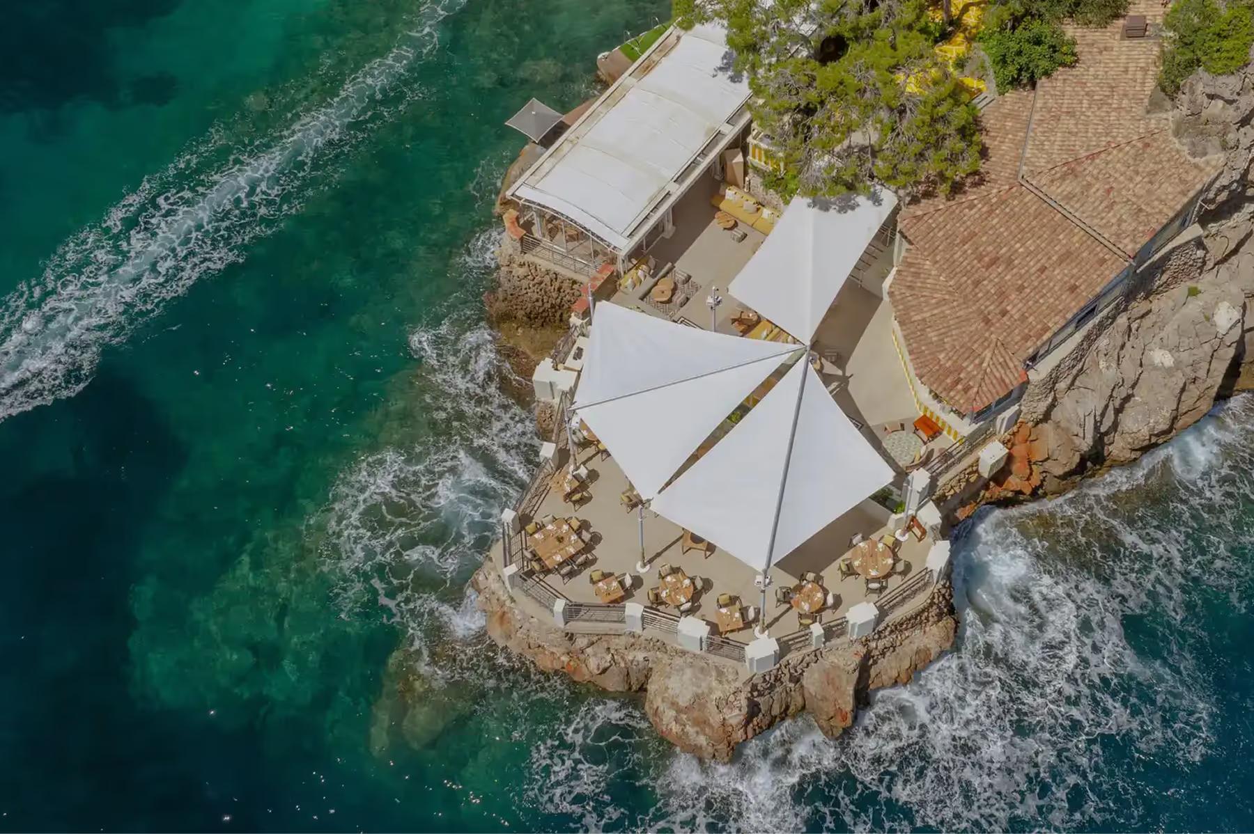 Hôtel de Paris Monte-Carlo: cliff-side beach area with white umbrellas overlooking green Mediterranean water