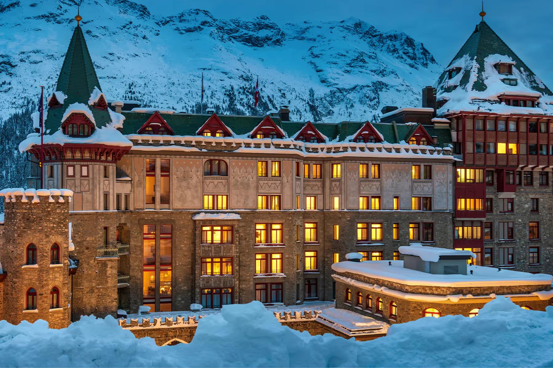 Badrutt’s Palace Hotel: illuminated hotel facade in evening snow with dark mountains behind
