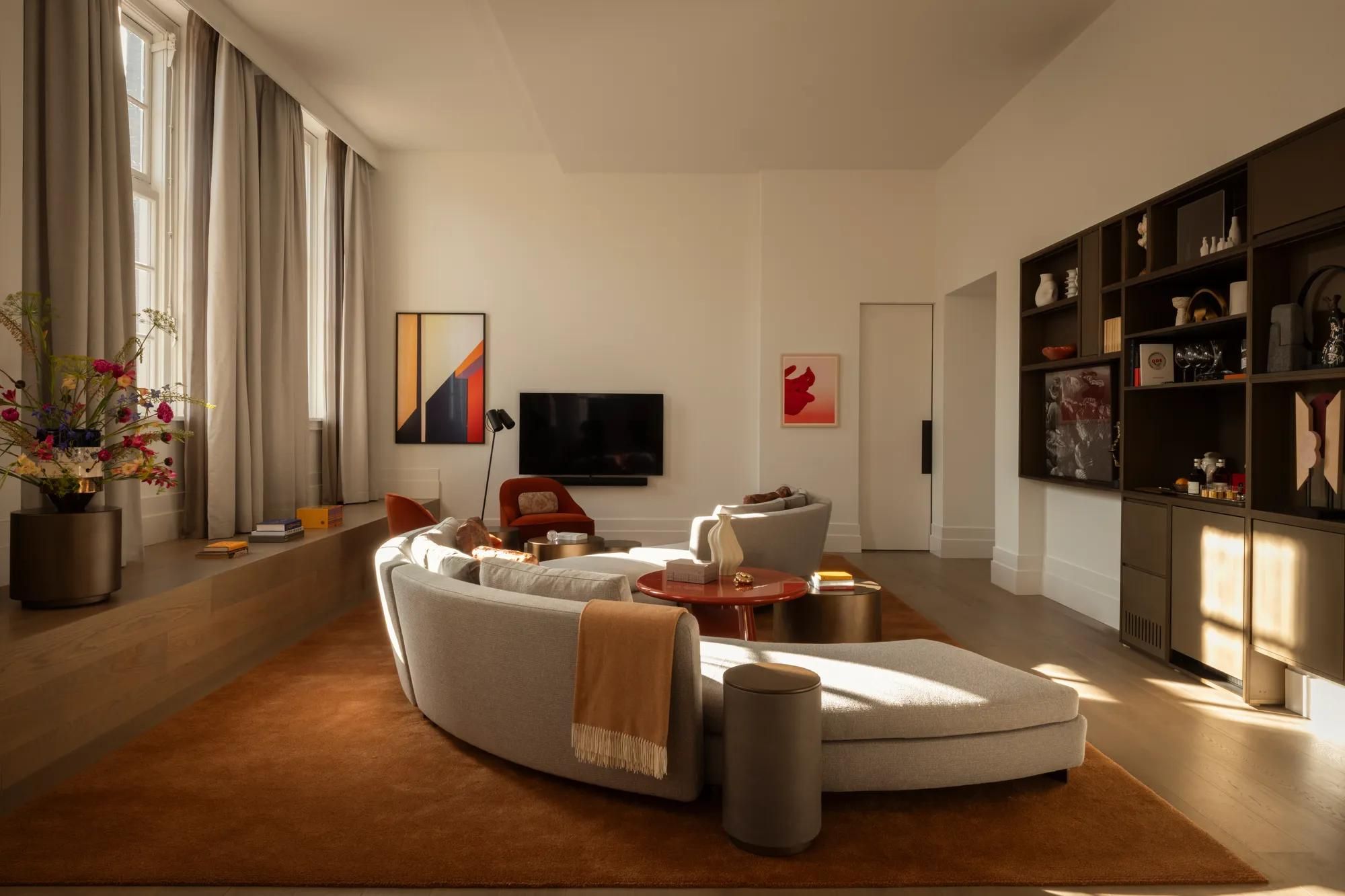 Rosewood Amsterdam: the Huis 020 living room with a curved sofa, open shelving, and tall windows