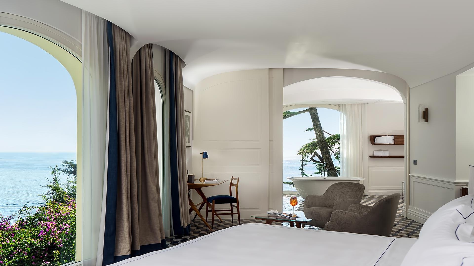 Bedroom with curved glass doors opening to seating area with sea views