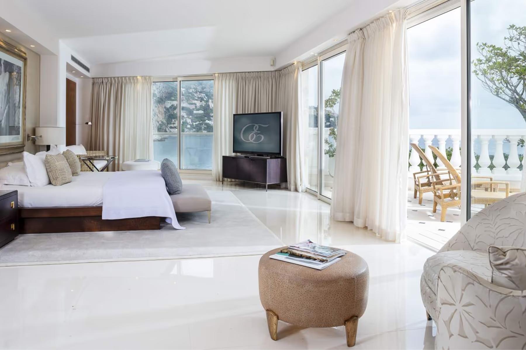 Hotel Cap-Estel: a bright bedroom with white furnishings, sheer curtains, and glass doors opening to sea views
