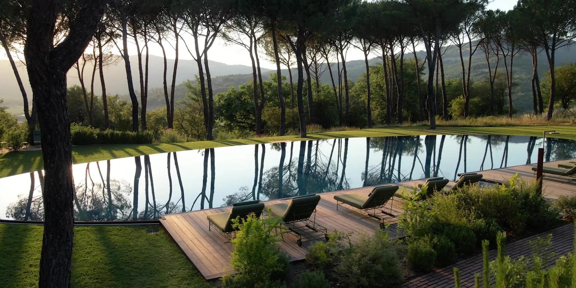 A reflecting pool framed by umbrella pines and a wooden sun deck, hills glowing gold beyond the trees