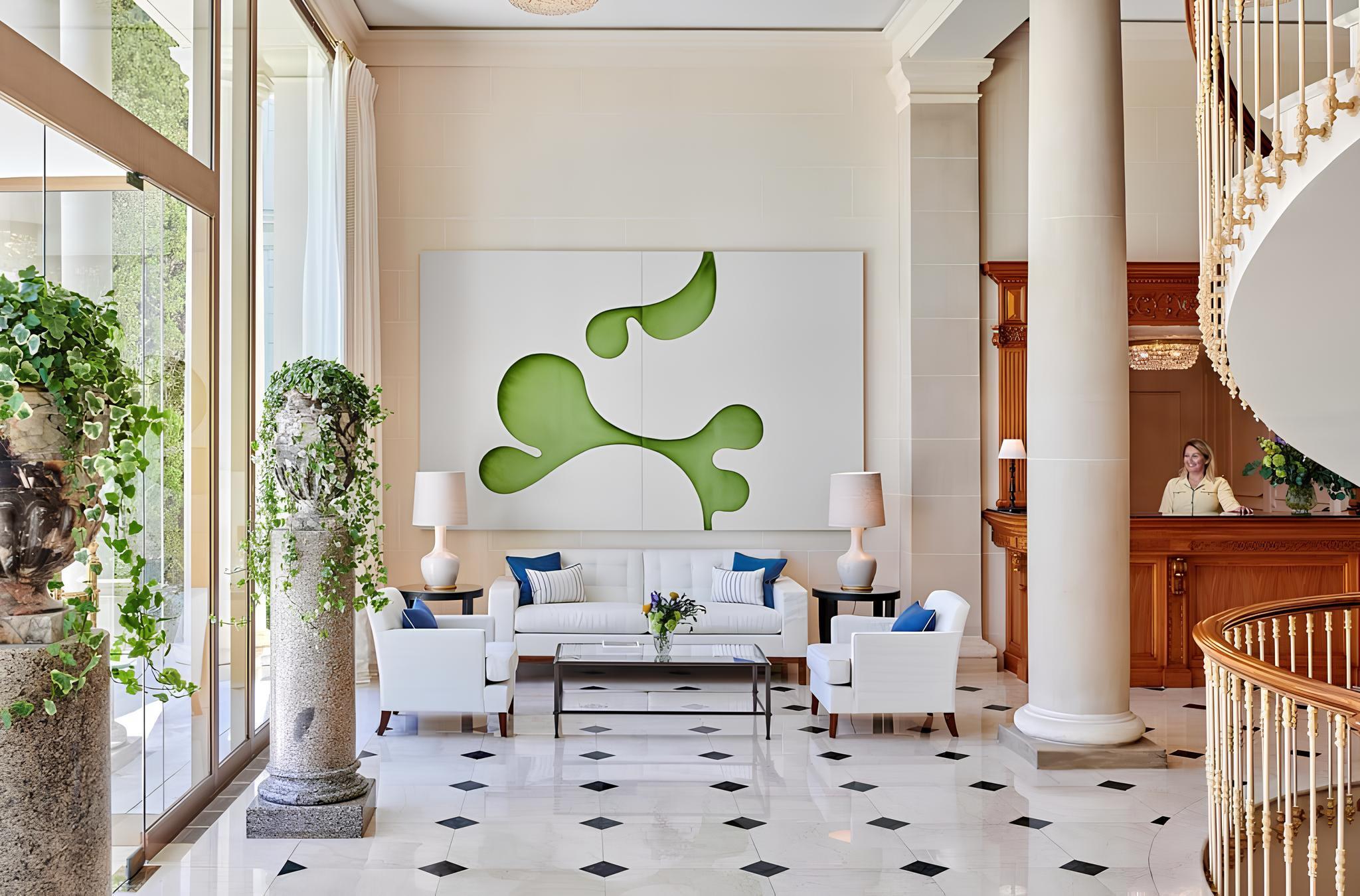 A high-ceilinged reception space with tall windows, arched artwork, seating areas, and terrazzo flooring
