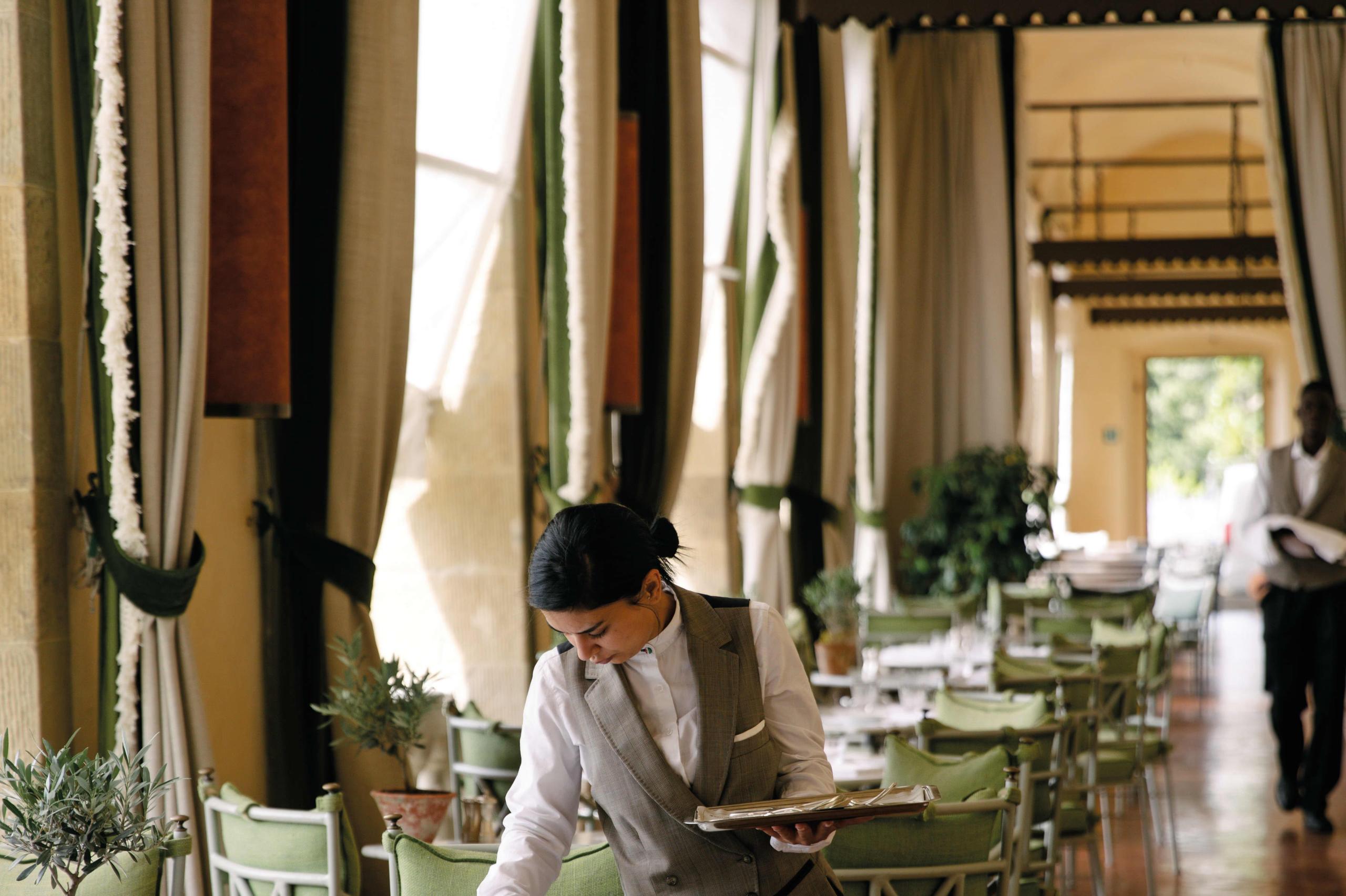 Villa San Michele: a server in white shirt working in a dining room with tall columns and draped fabric