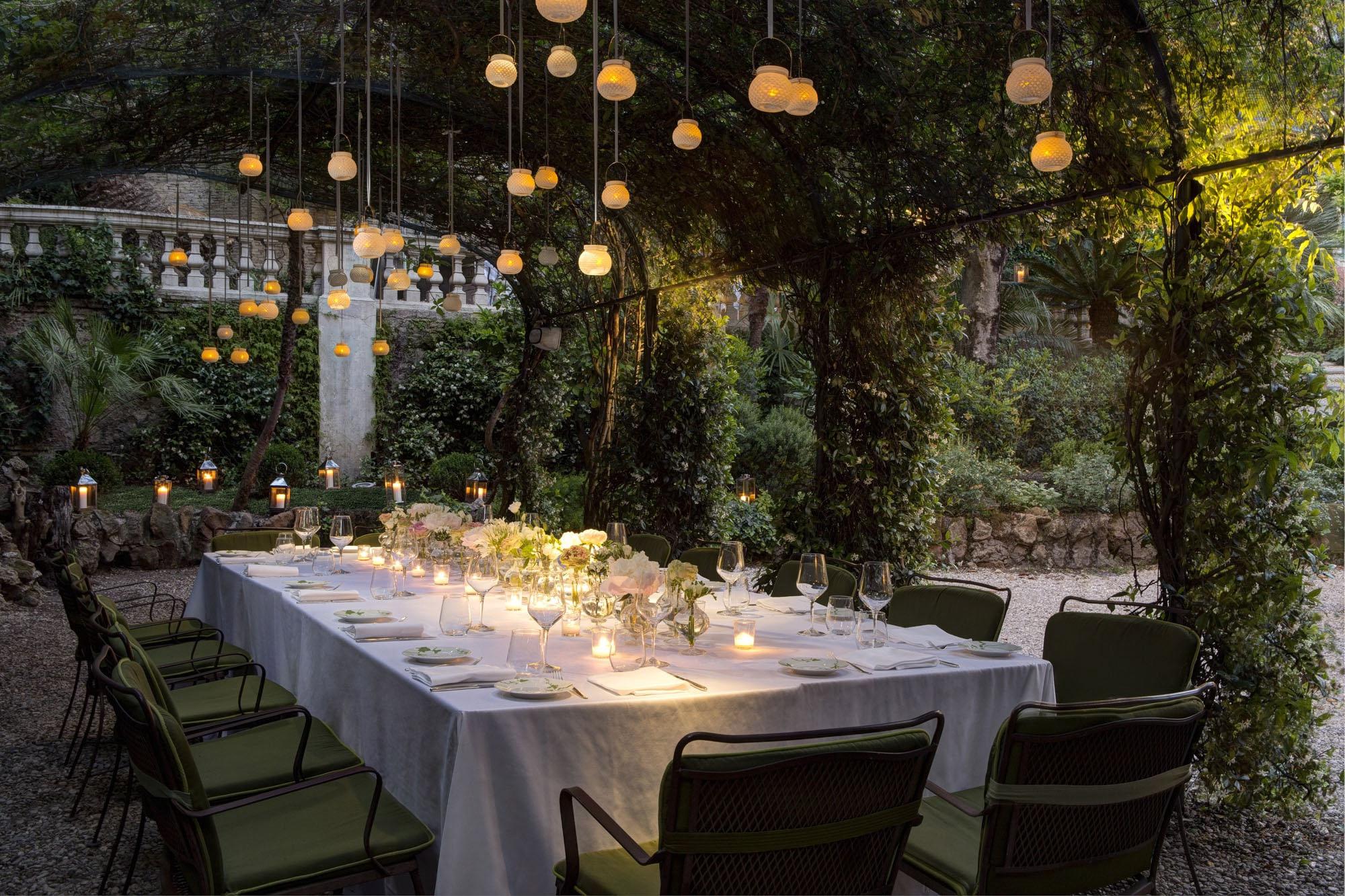 Outdoor table under hanging pendant lights with ivy and lush surroundings at night