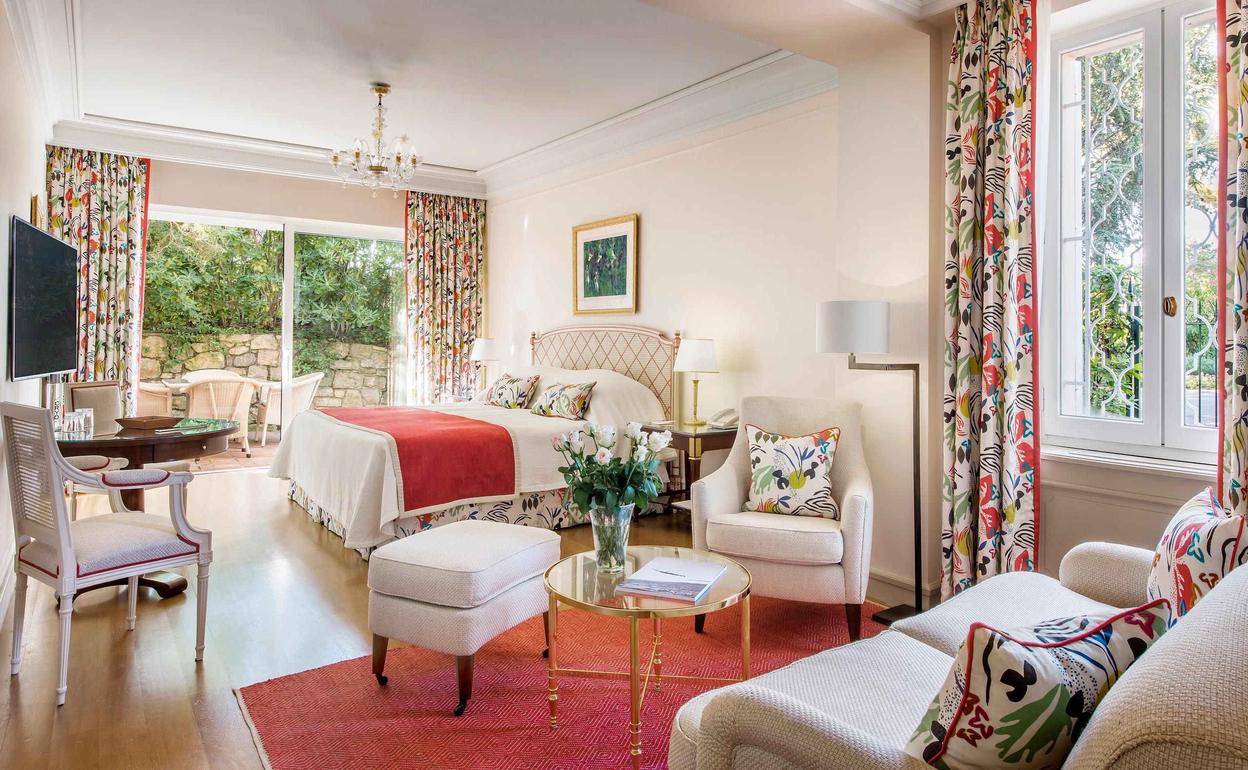 Hôtel du Cap-Eden-Roc: a guest room with red upholstered furniture, white walls, coral drapery, and traditional furnishings