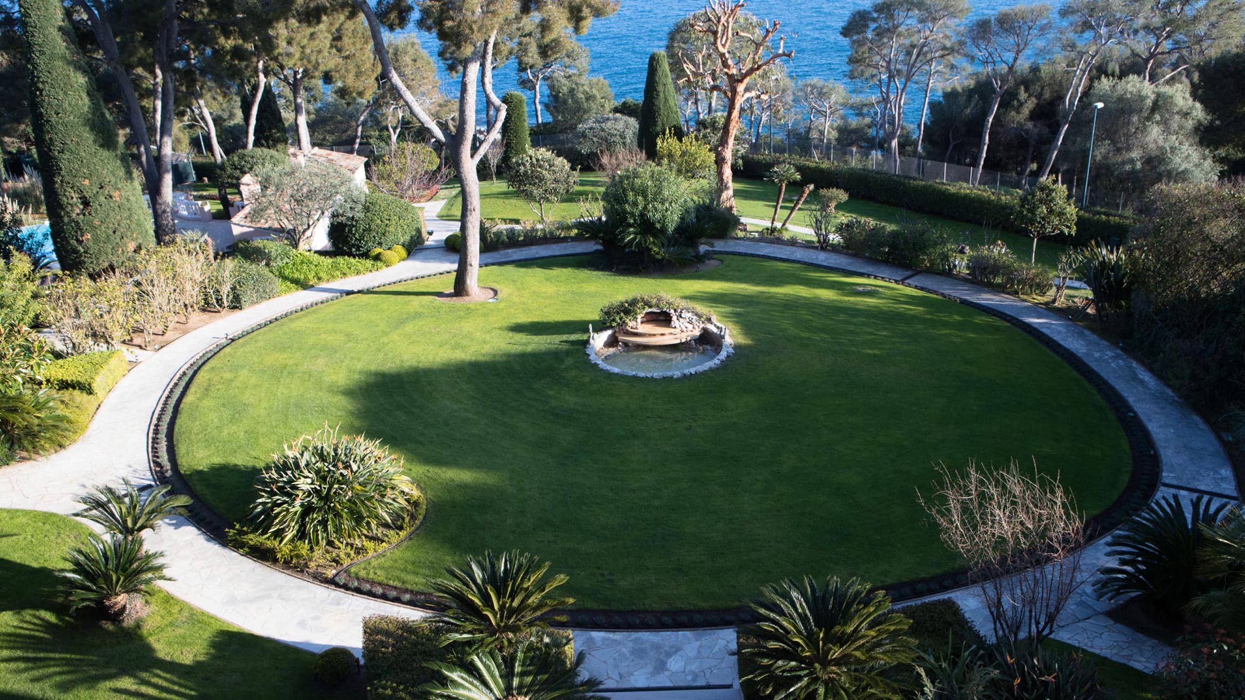 Grand-Hôtel du Cap-Ferrat: circular lawn with central fire pit, trees, and sea view beyond